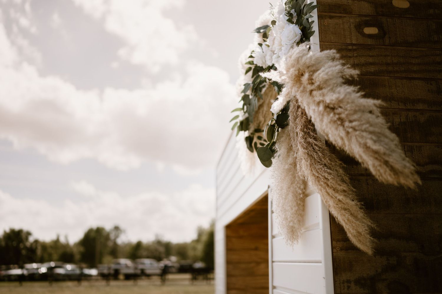 Decorative dried pampas grass wedding decor against wooden barn wall.