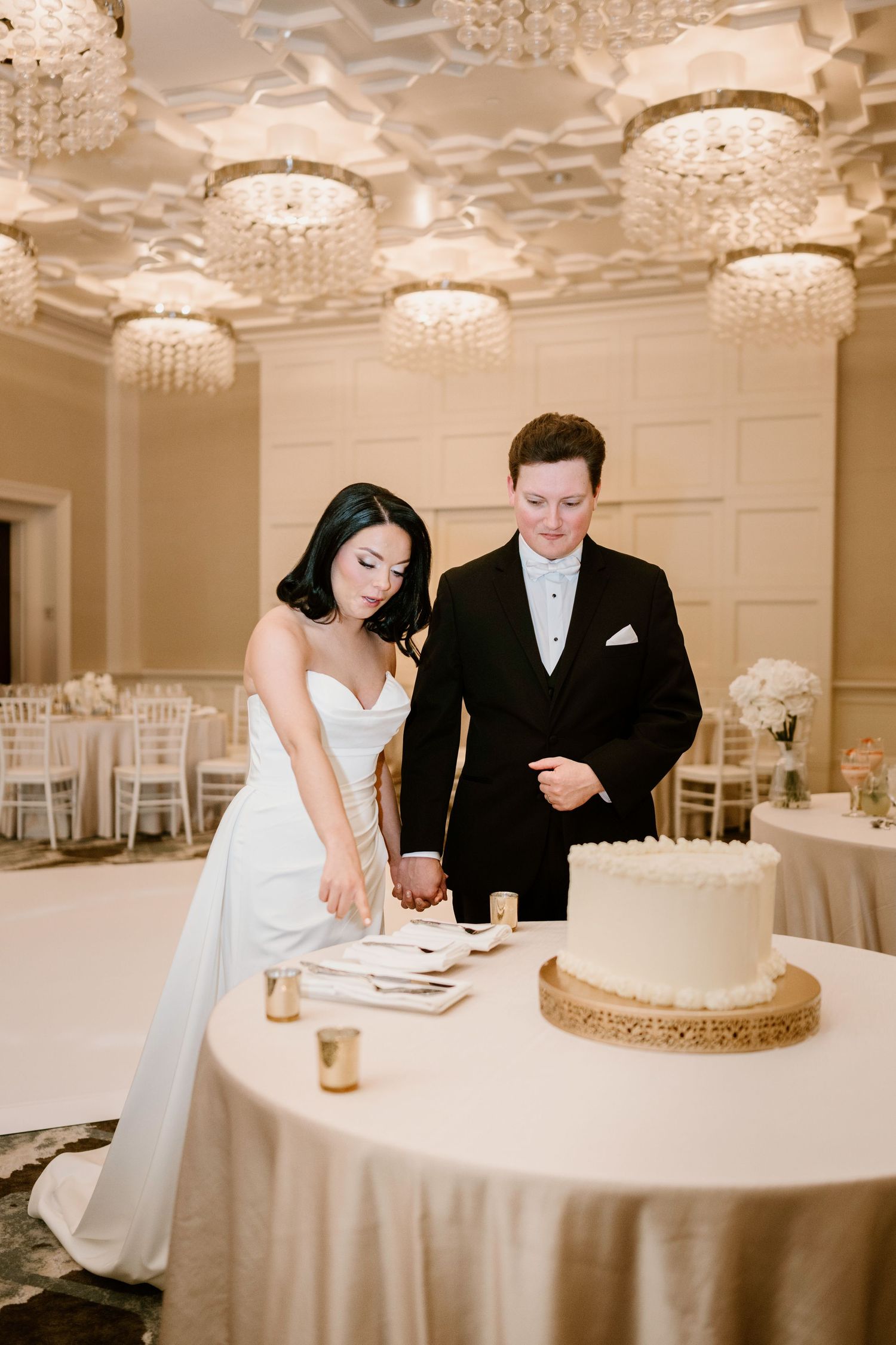 Wedding couple cutting their elegant white cake in a beautifully lit reception room.
