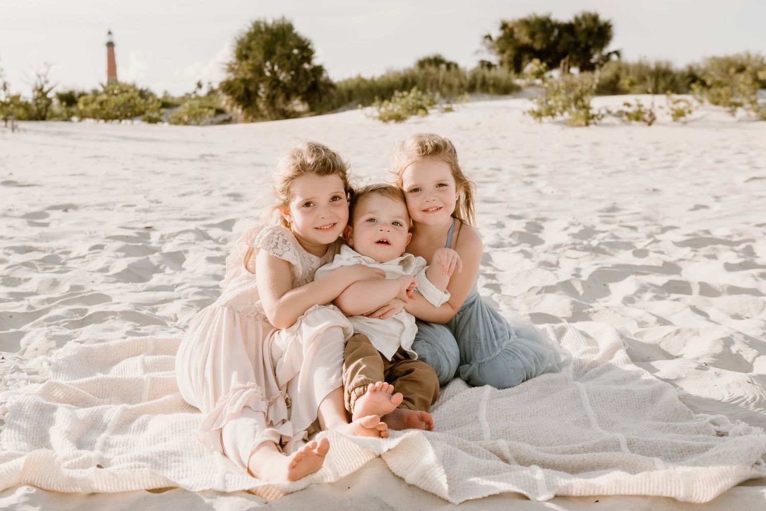 A family group cuddles together on white sand during a beach portrait session.