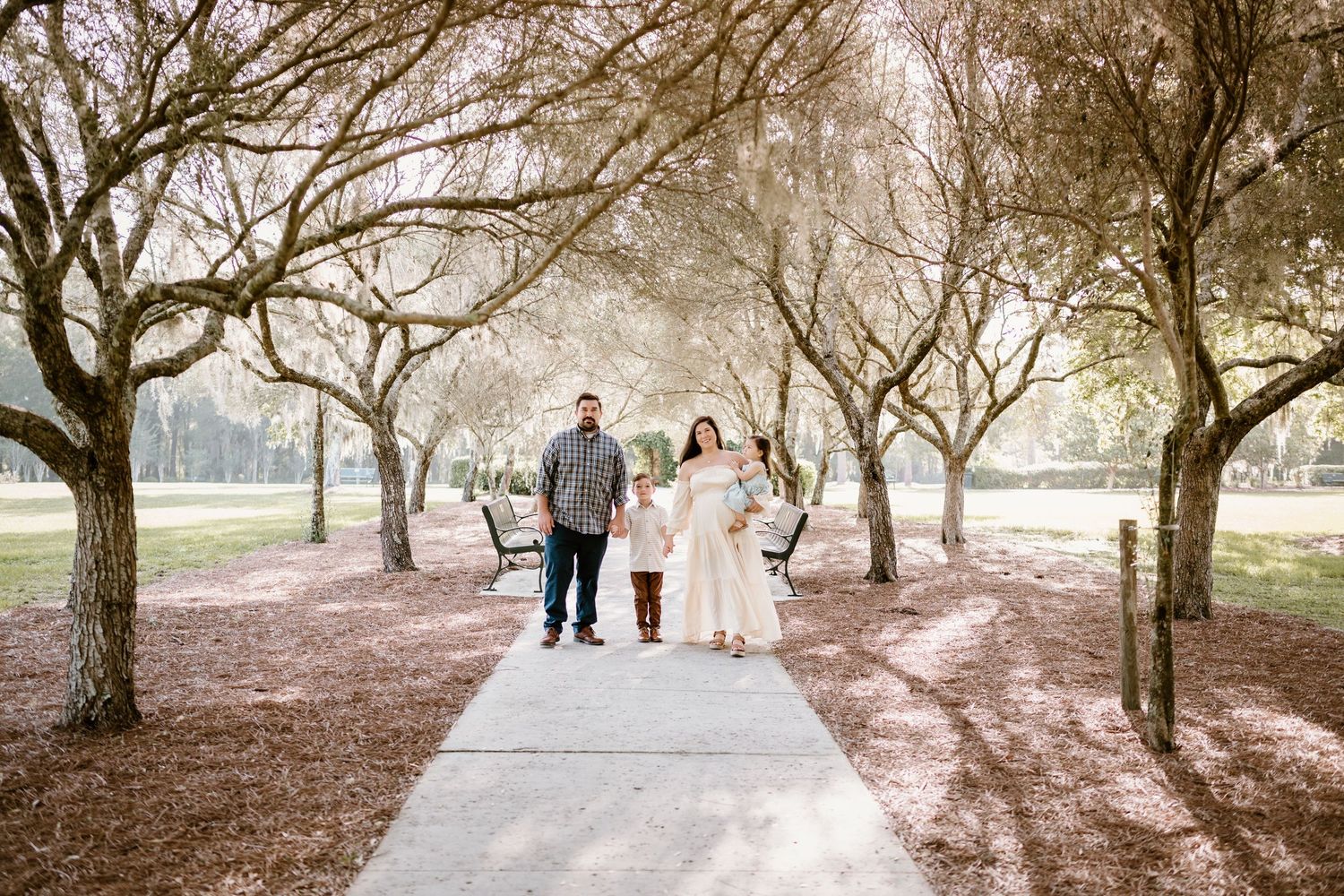 Three people walk along a tree-lined path during a photo session.