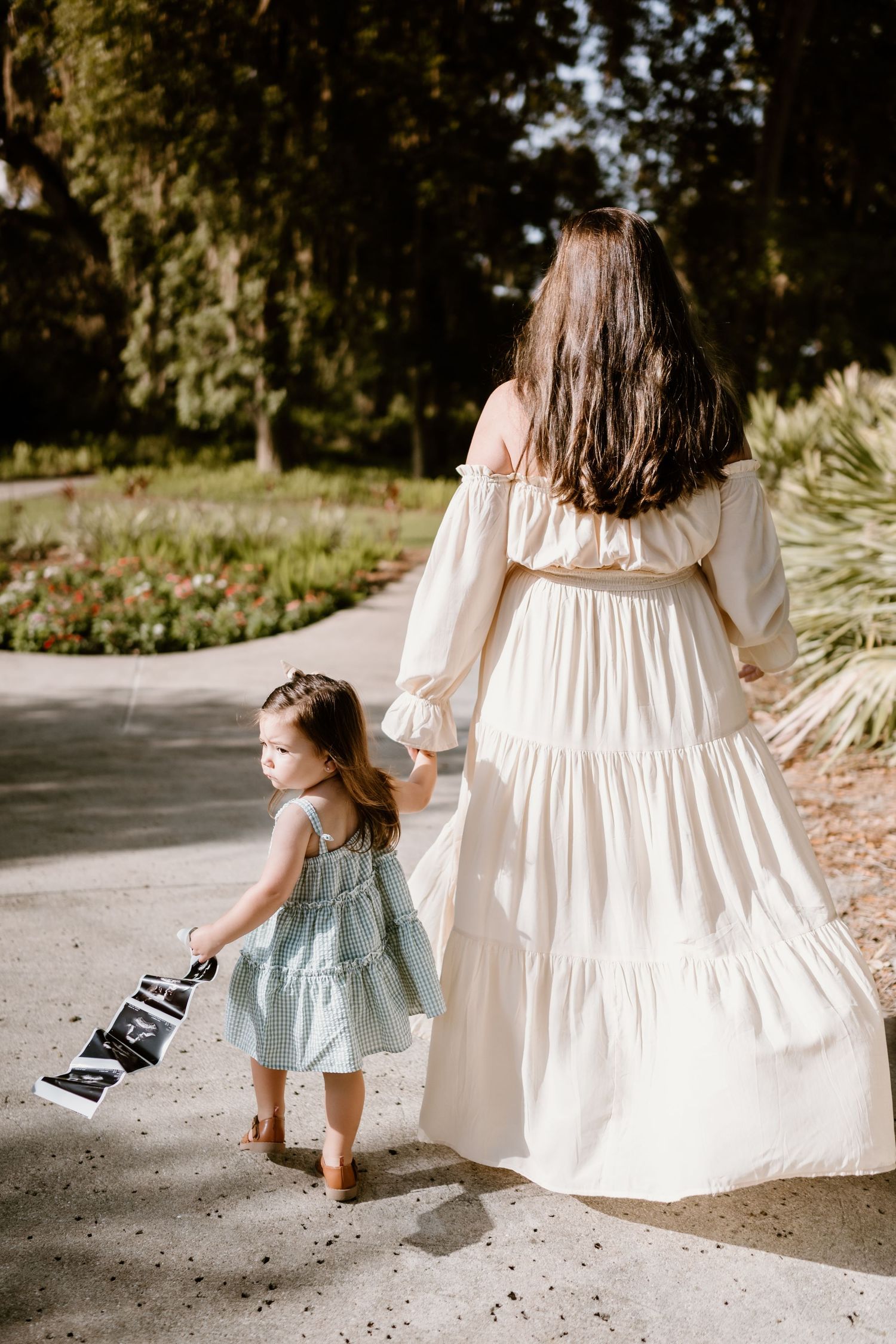 Young child walking with someone in a white dress while holding a vintage camera.