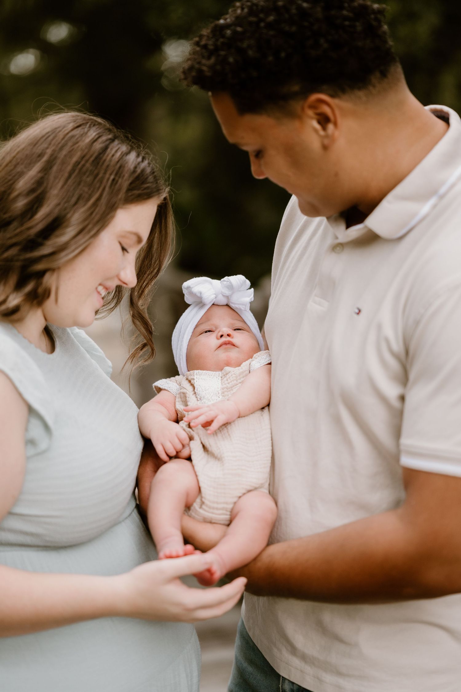 Intimate family portrait captures parents bonding with their newborn baby in soft natural light.