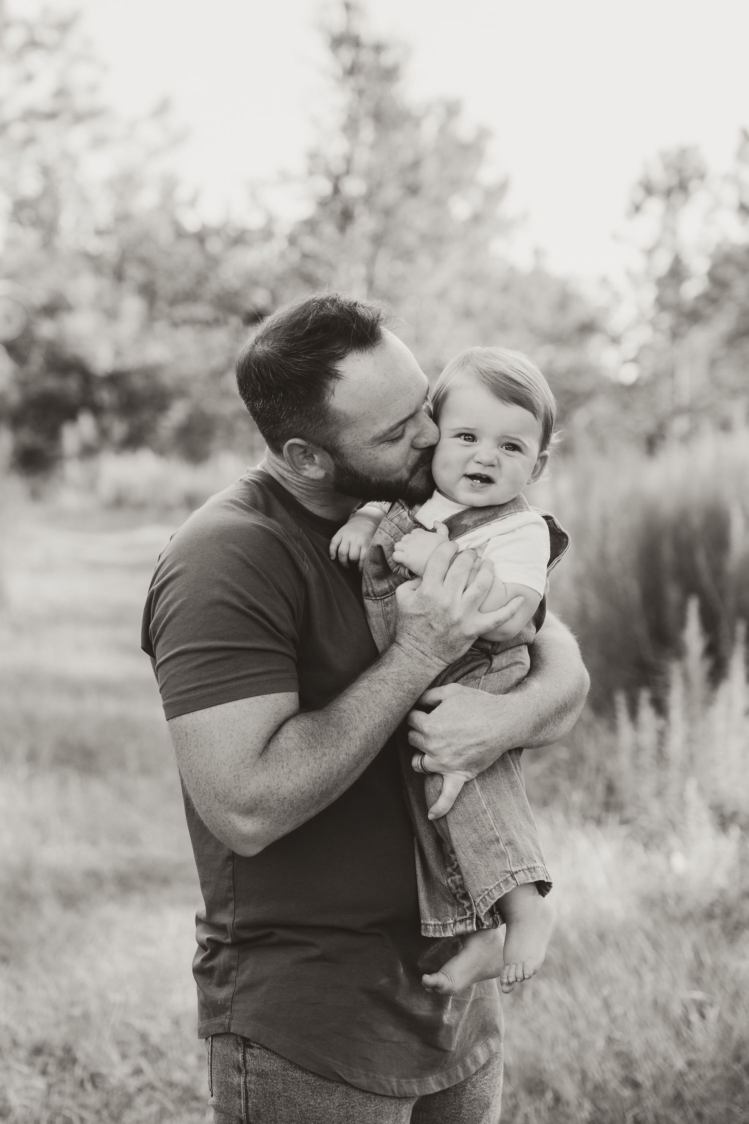 Black and white portrait of parent sharing an affectionate moment with baby in a field.