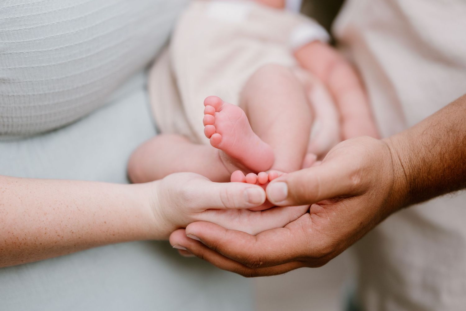 Close-up detail shot of tiny baby feet being held by gentle hands.