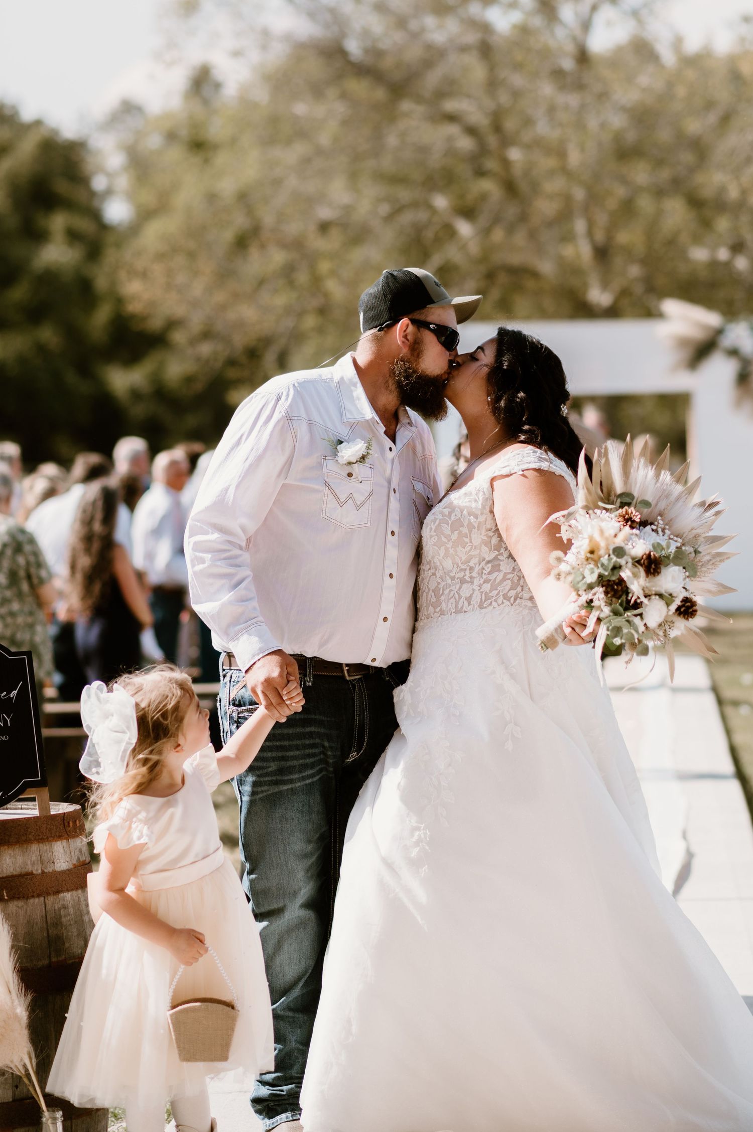 Sweet moment between newlyweds and young flower girl during outdoor wedding celebration.