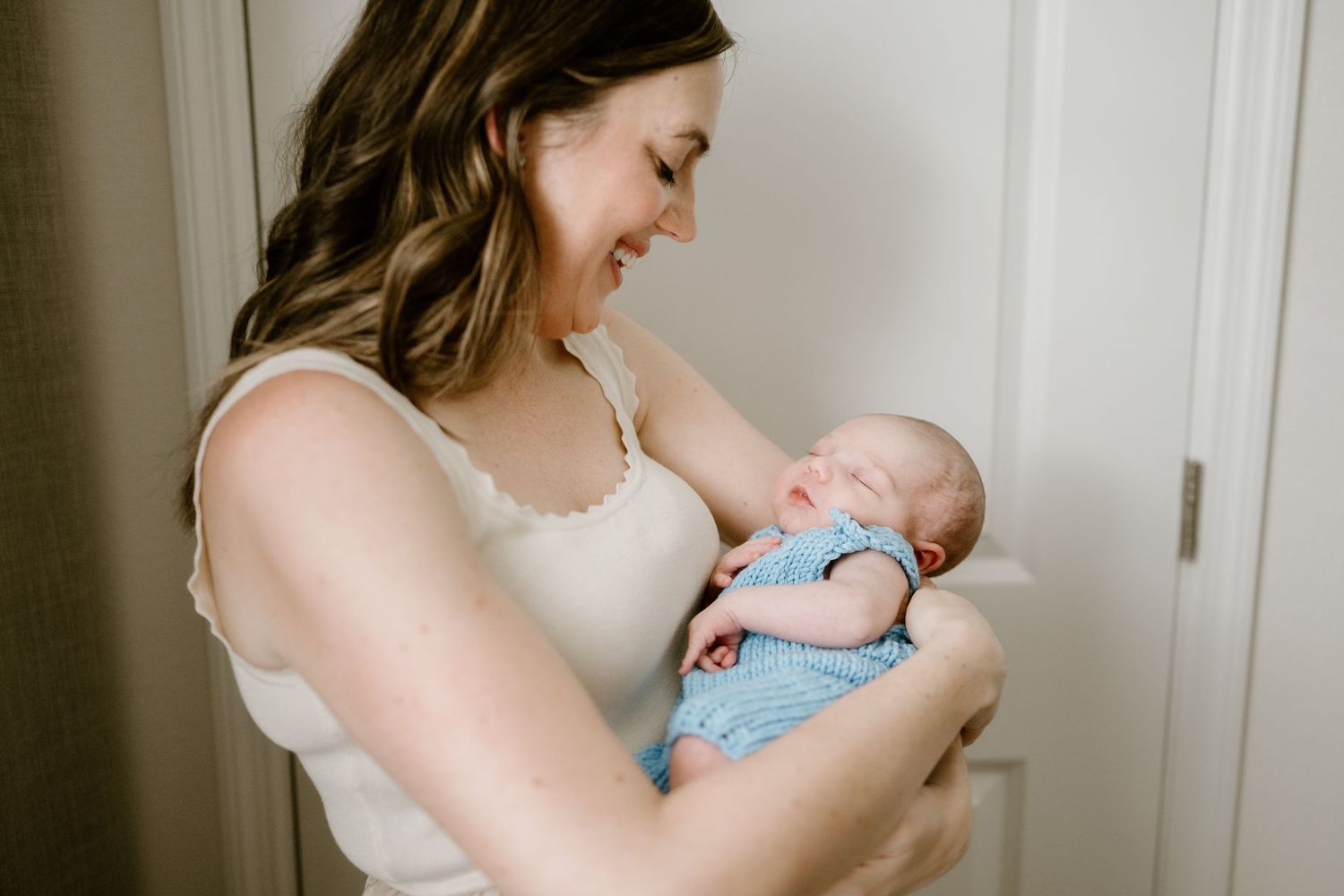 A peaceful newborn rests in loving arms while wearing a delicate blue outfit.