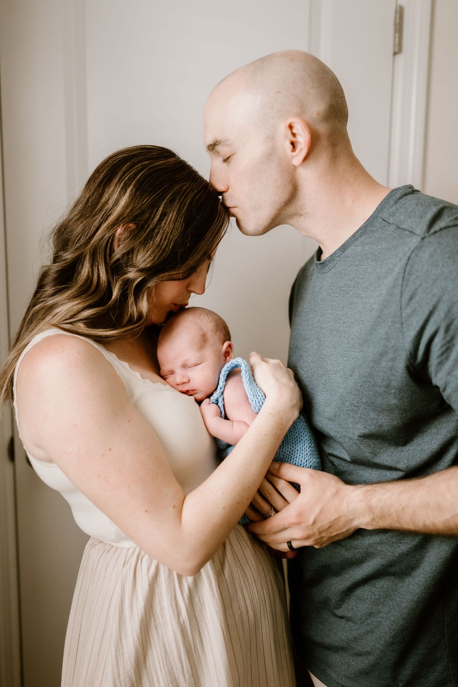 Parents sharing loving moments with their newborn in a series of intimate indoor portraits.