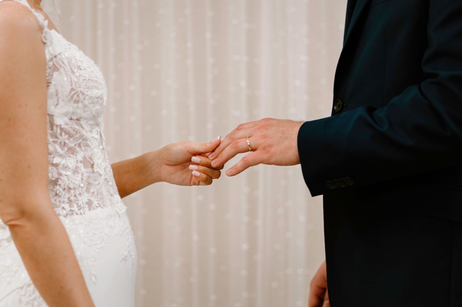 Wedding ceremony moment showing hands exchanging rings against white backdrop.