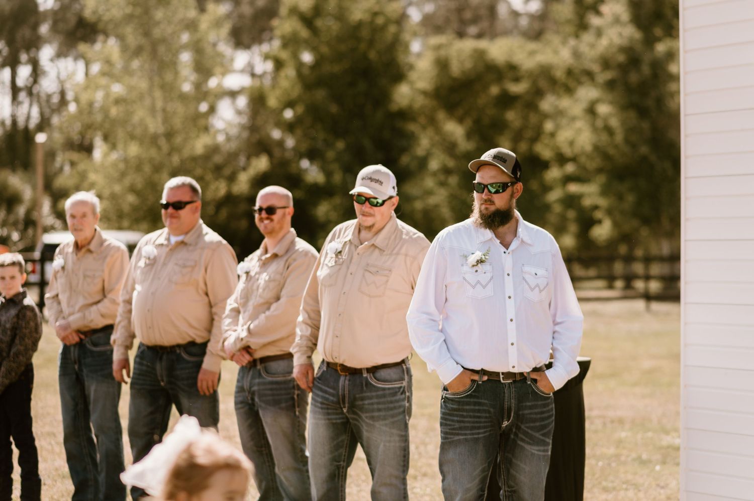 Groomsmen in matching attire standing in line at outdoor wedding.