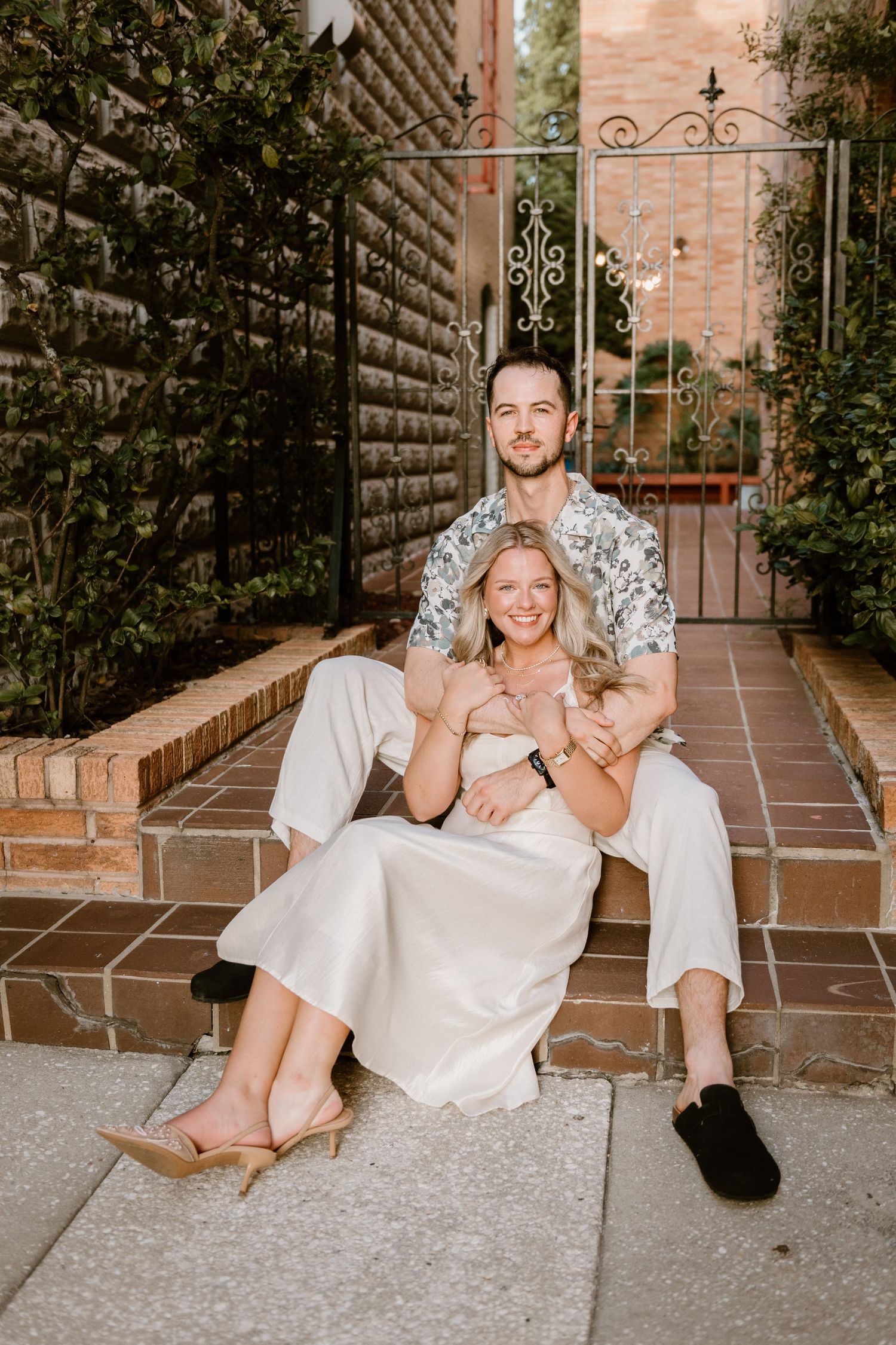 Couple laughing together while sitting on terracotta tiles in a brick-lined courtyard.