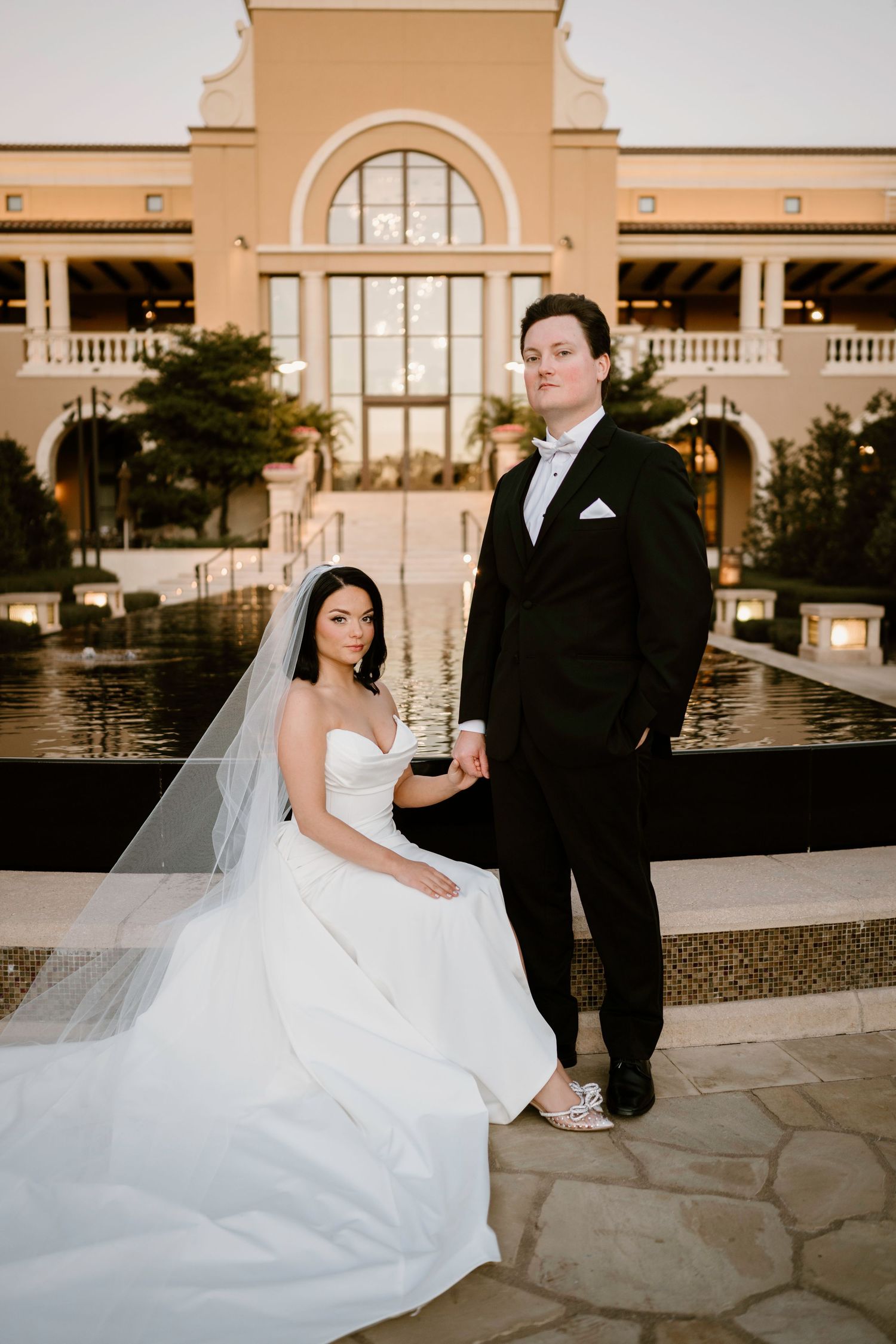 Wedding couple shares tender moment by illuminated resort fountain at dusk.