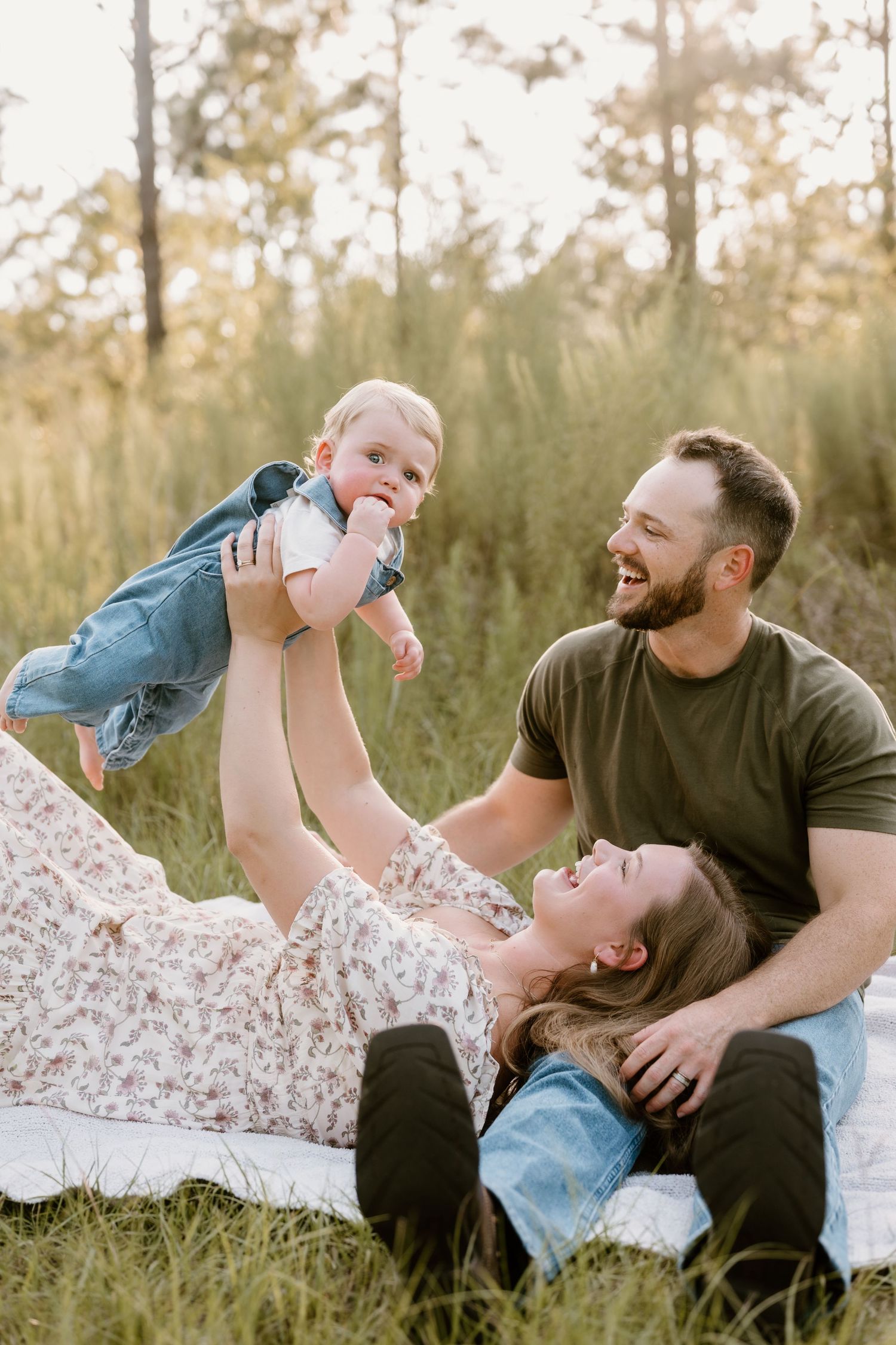 A joyful family moment captured outdoors with a baby being lifted playfully in a grassy field.