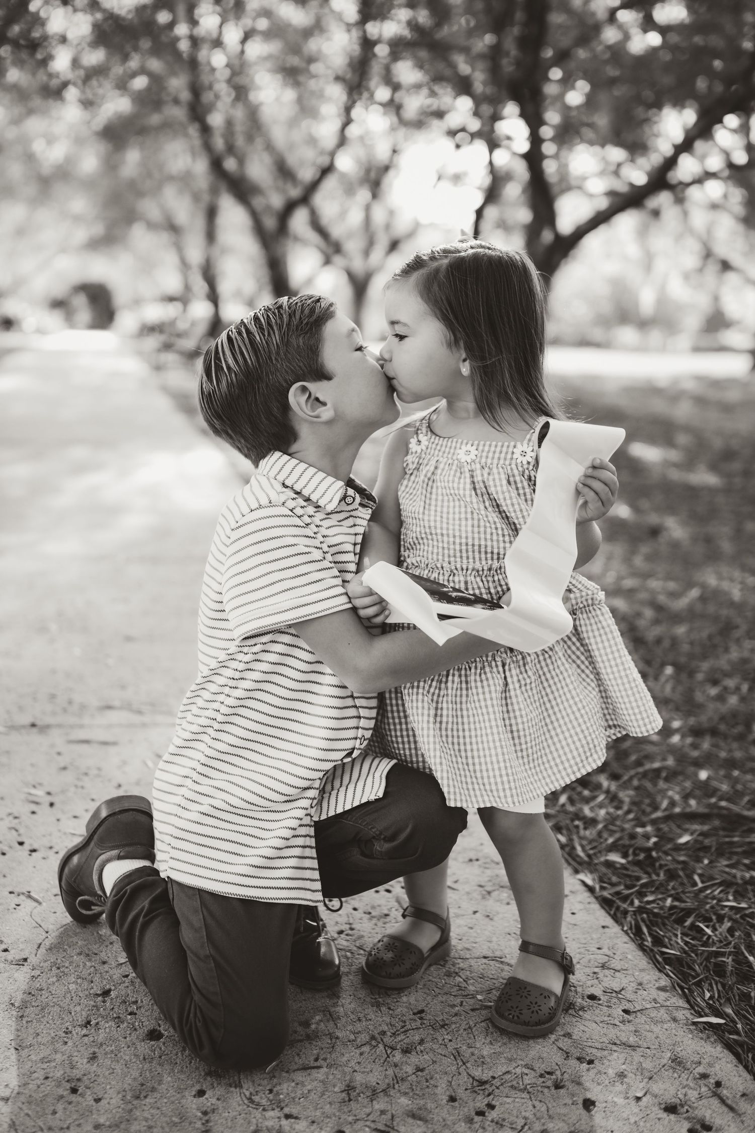 Two children sharing a tender moment under trees in black and white photography.