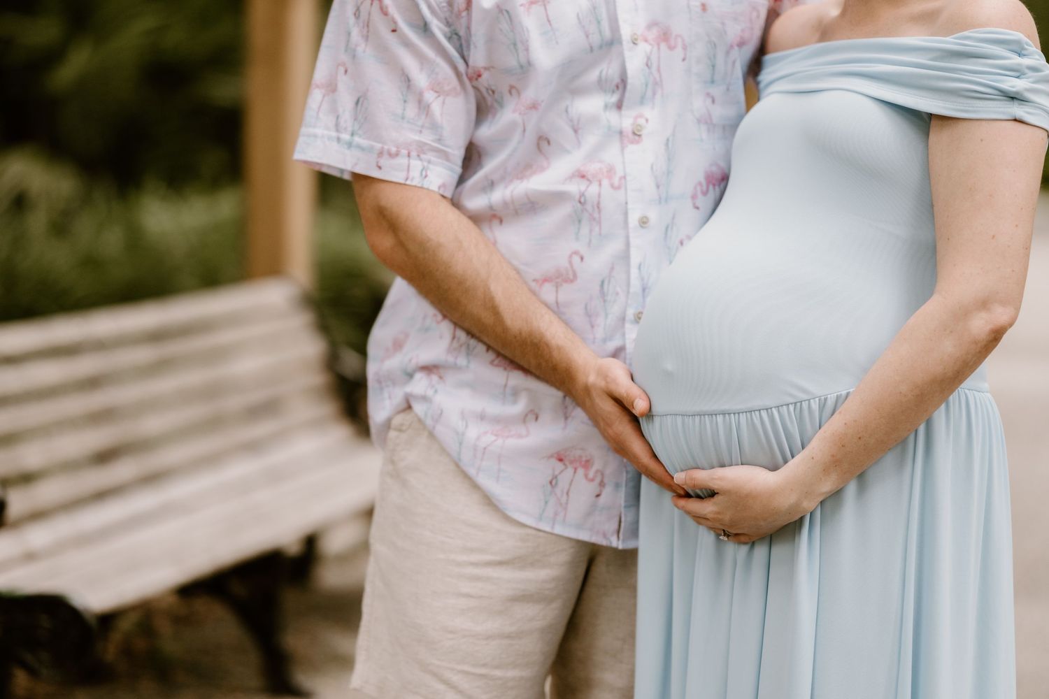 Close-up shot of a pregnant belly in a light blue dress with hands gently cradling it.