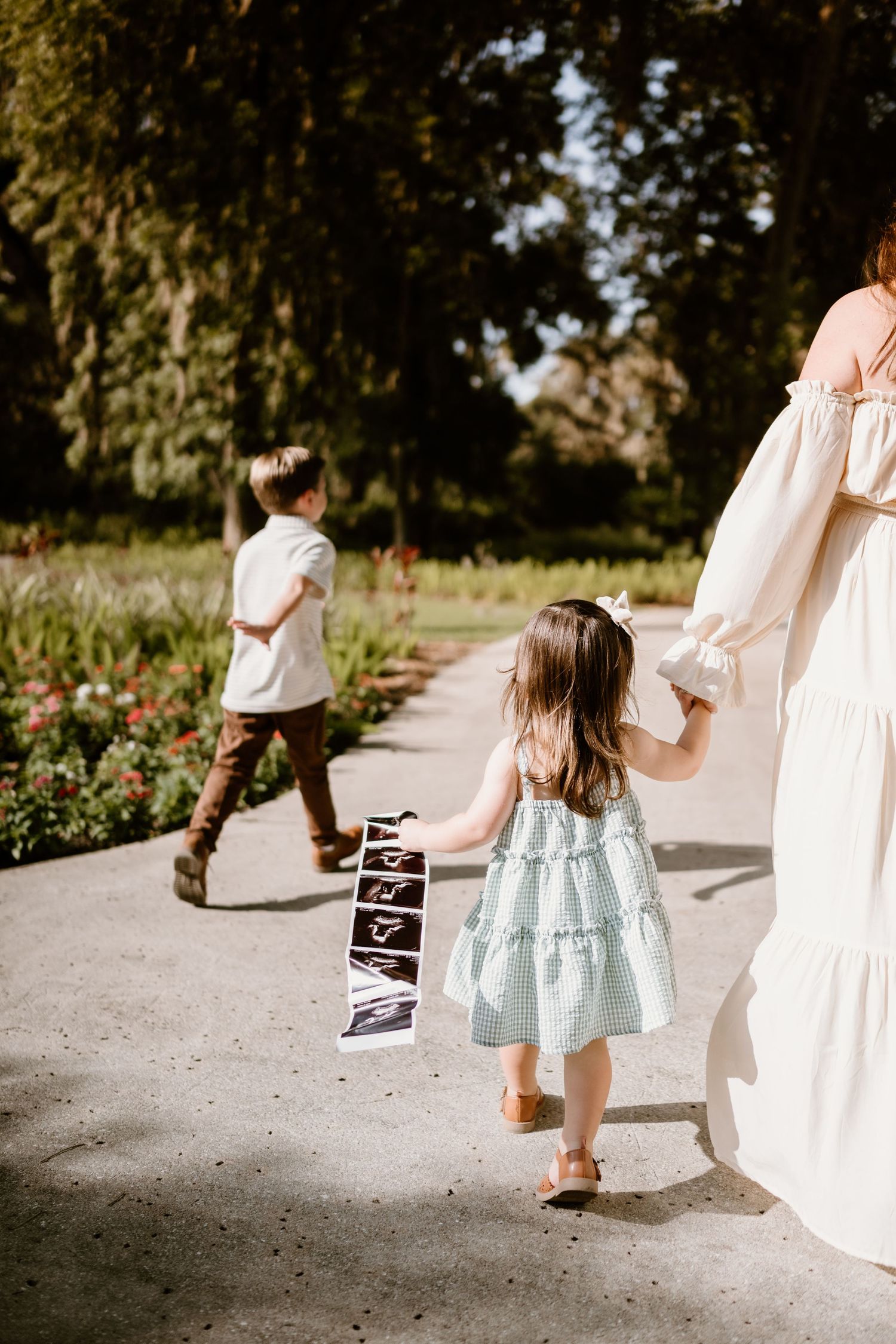 Child in light blue dress walking with someone in white dress along a garden path.