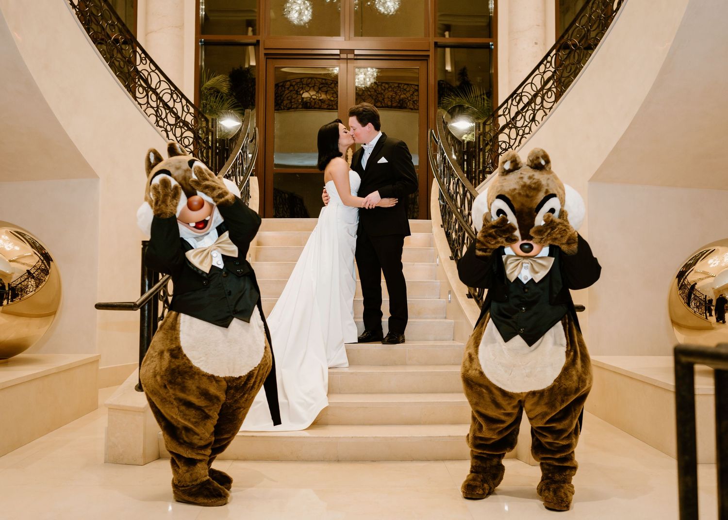 A wedding couple shares a moment on grand stairs while Disney chipmunk characters pose in the foreground.