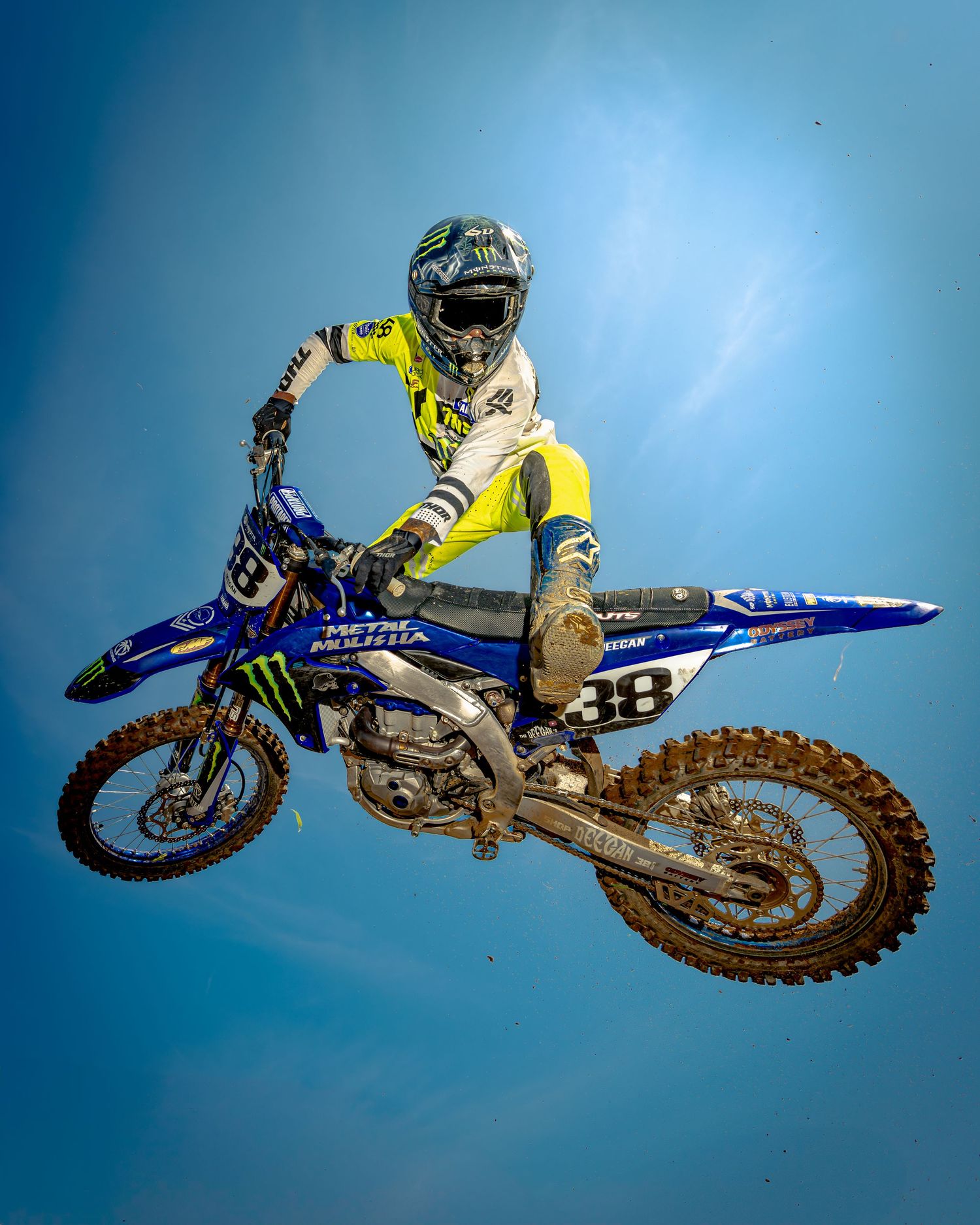 Motocross rider executing aerial stunt against blue sky background showing sequential movements.