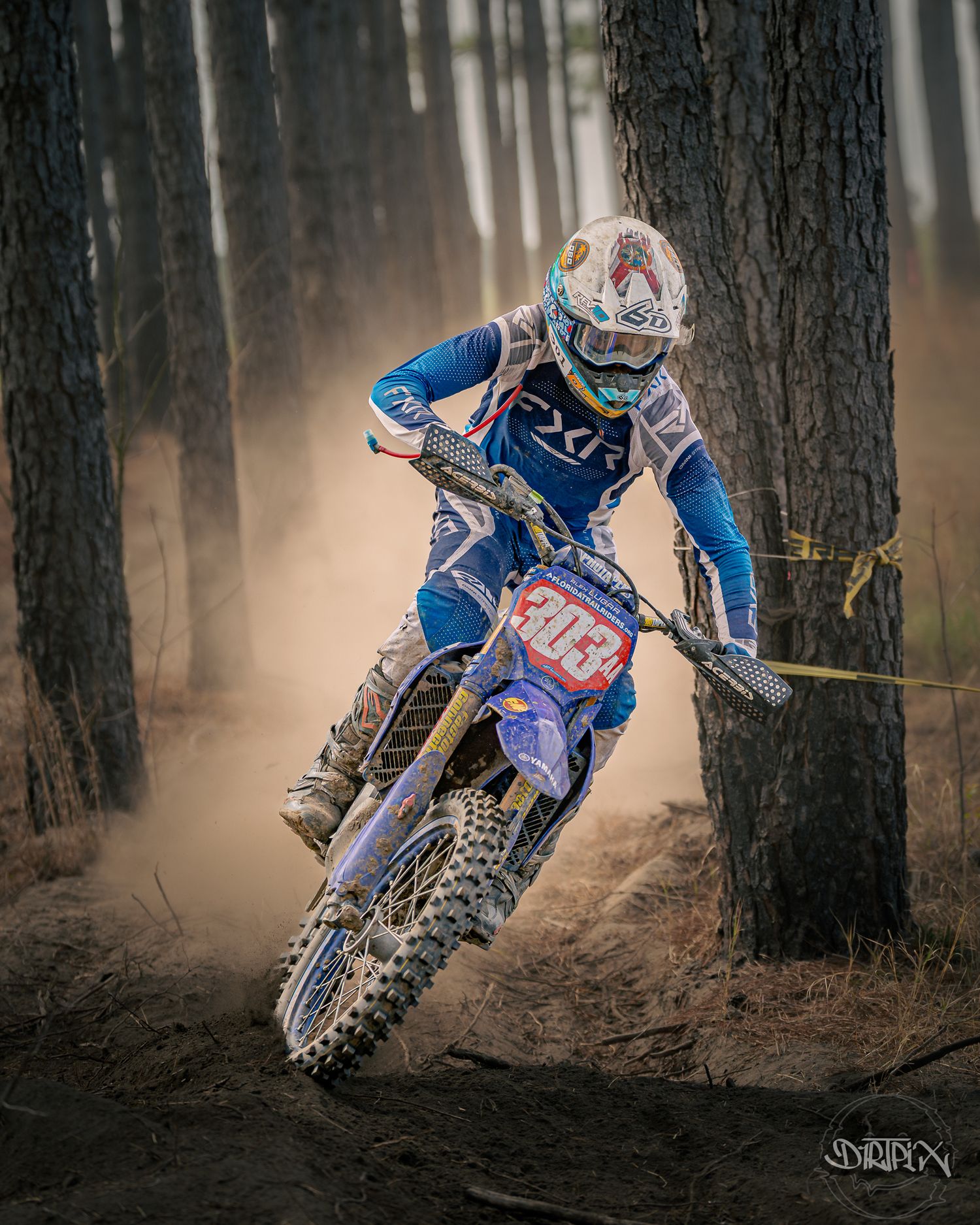 Motocross rider navigates through a dusty forest trail during intense off-road racing competition.