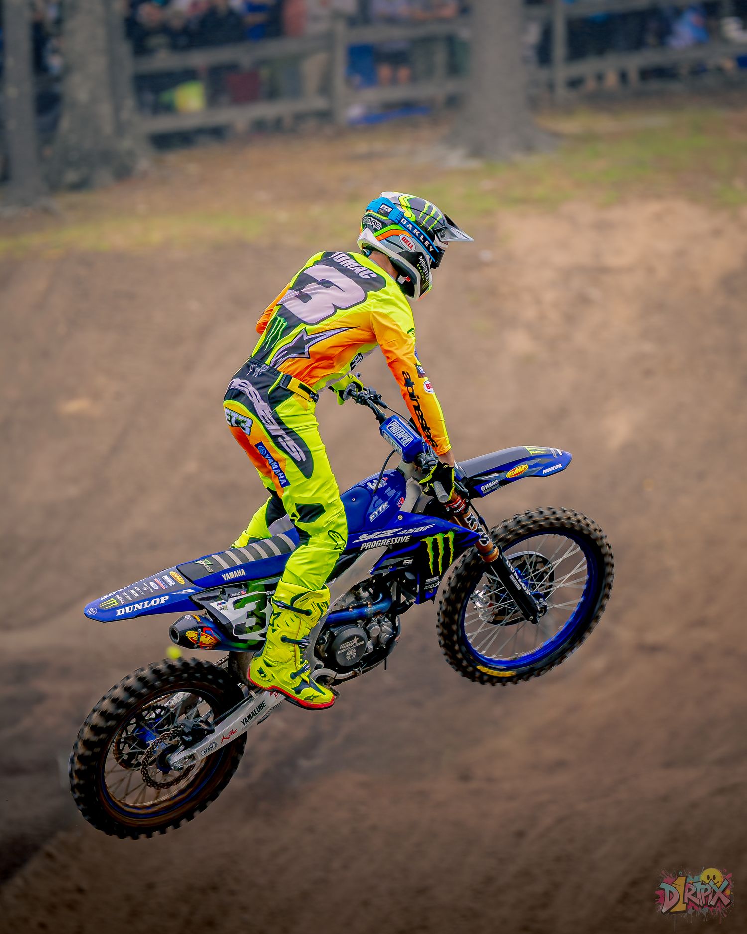 Dirt bike rider in bright gear performing aerial maneuver on outdoor track.
