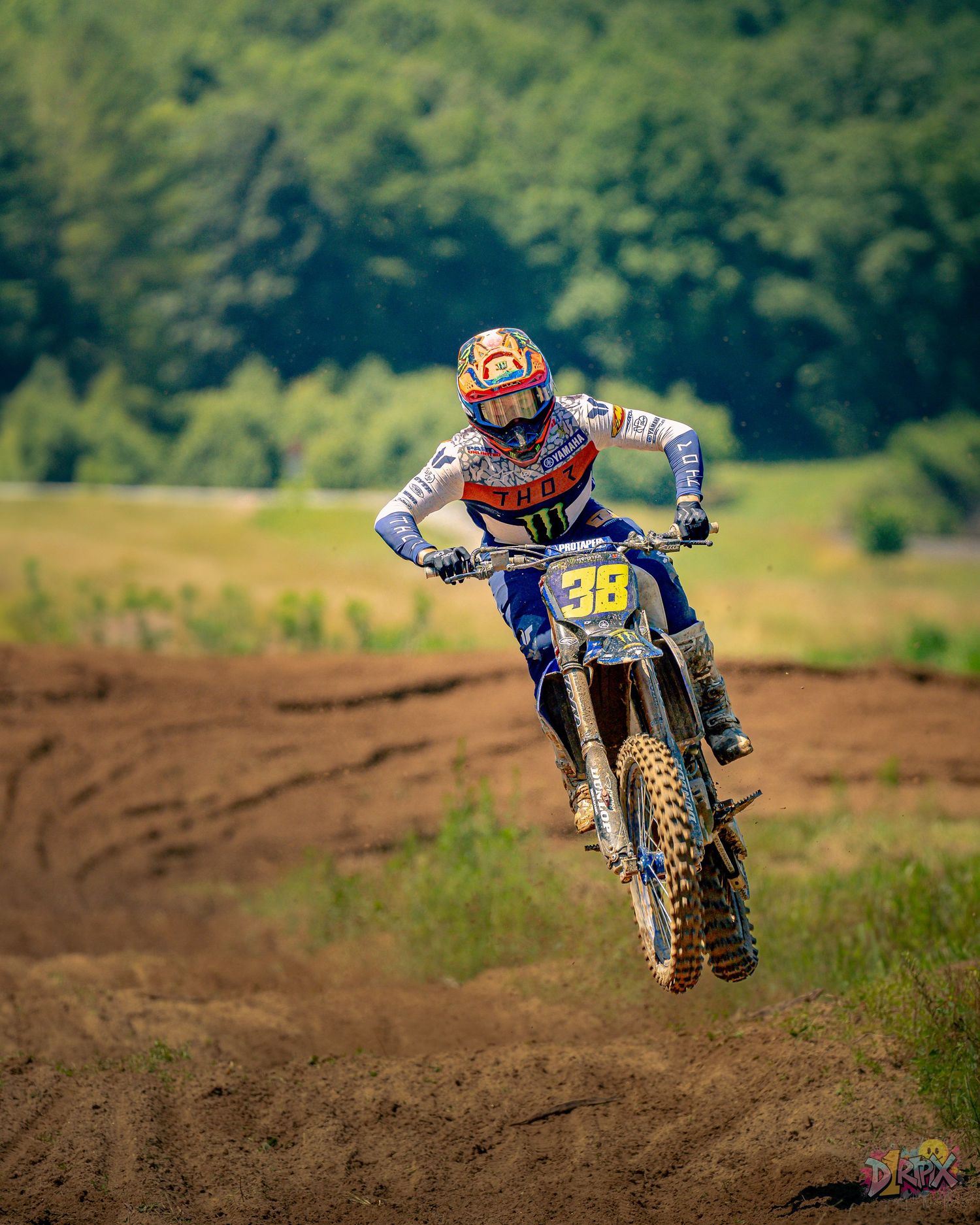 Motocross riders catching air off dirt jump during daytime race.