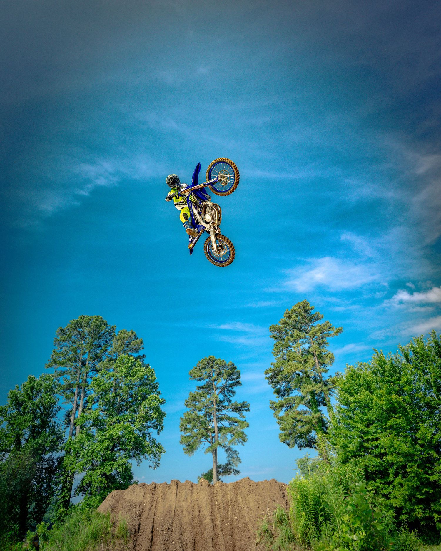 Sequential shots of motocross bike performing backflip trick over dirt jump with blue sky background.