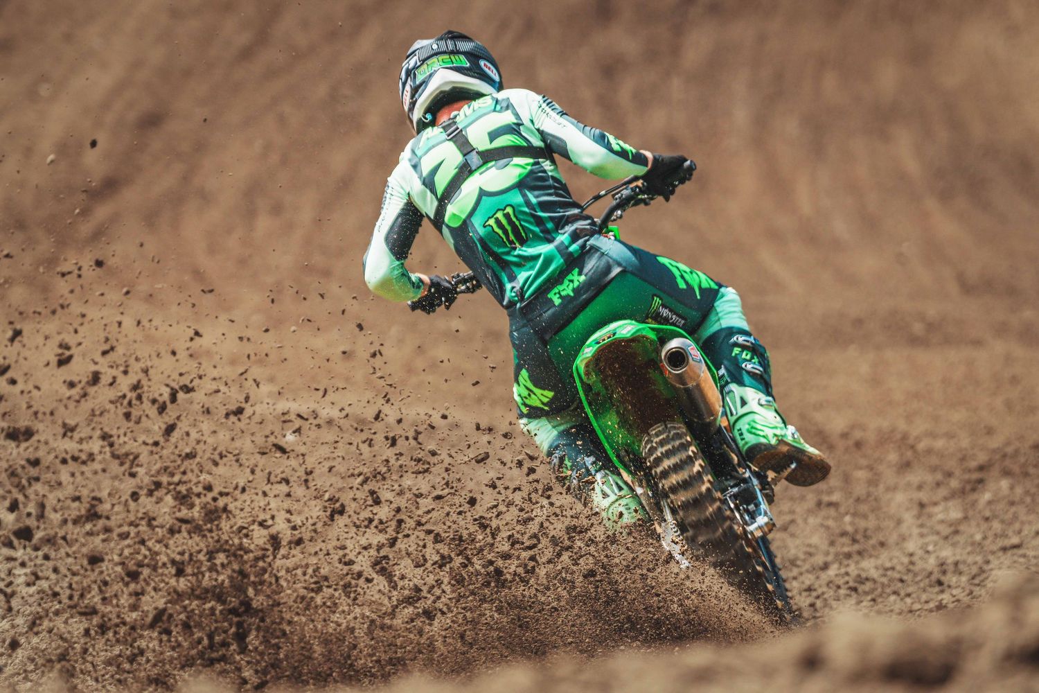 Motocross rider in green gear navigating a dirt track on a green dirt bike, spraying mud mid-race.