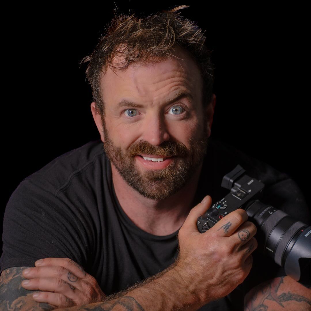 A photographer in a black shirt shows a range of playful expressions while posing with a camera against a dark background.