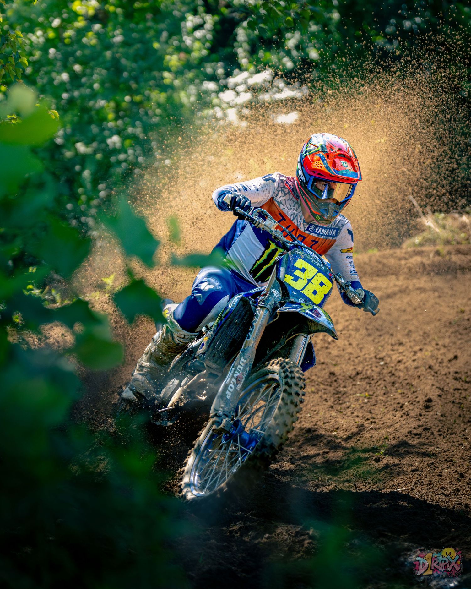 Dirt bike spraying roost while accelerating through corner on motocross track.
