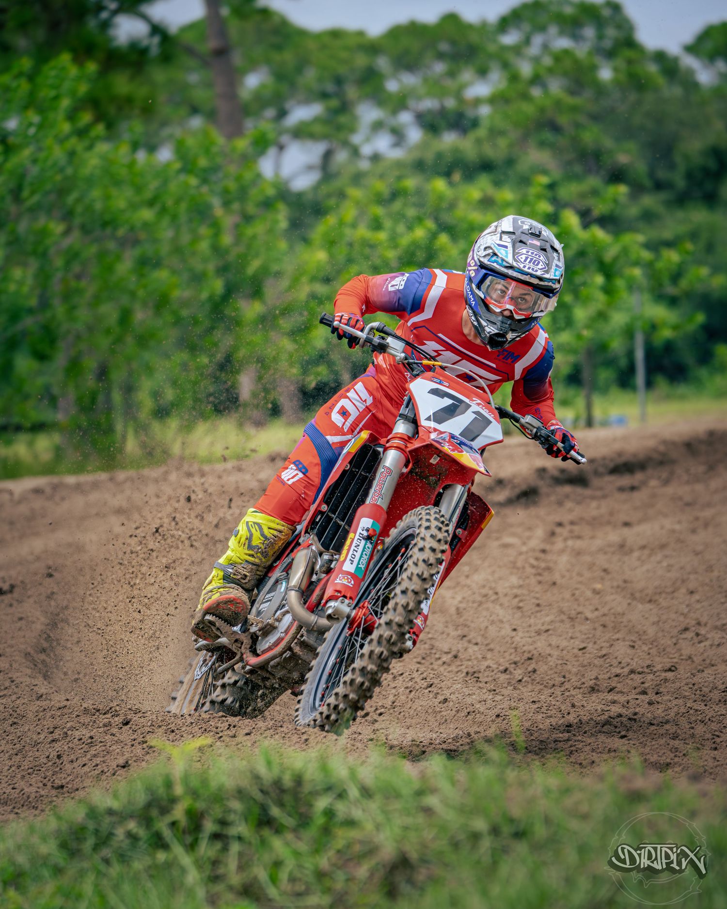 Red motocross bike cornering aggressively on dirt track with dramatic lean angle.