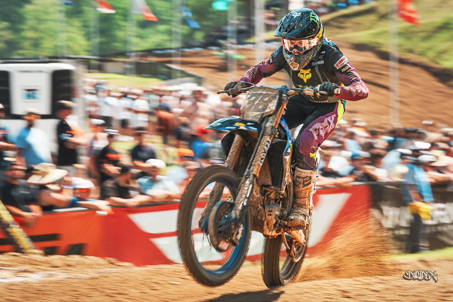 Motocross rider racing on a dirt track at an outdoor competition, wearing protective gear on a dirt bike.