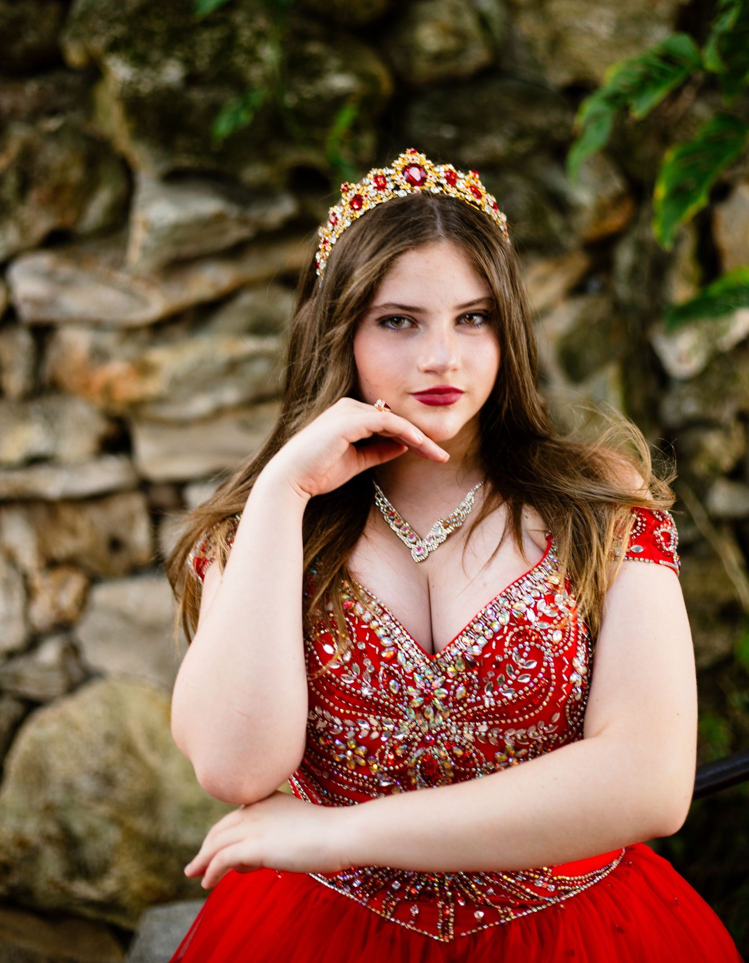 Red crystal-embellished ballgown photographed against textured stone wall.