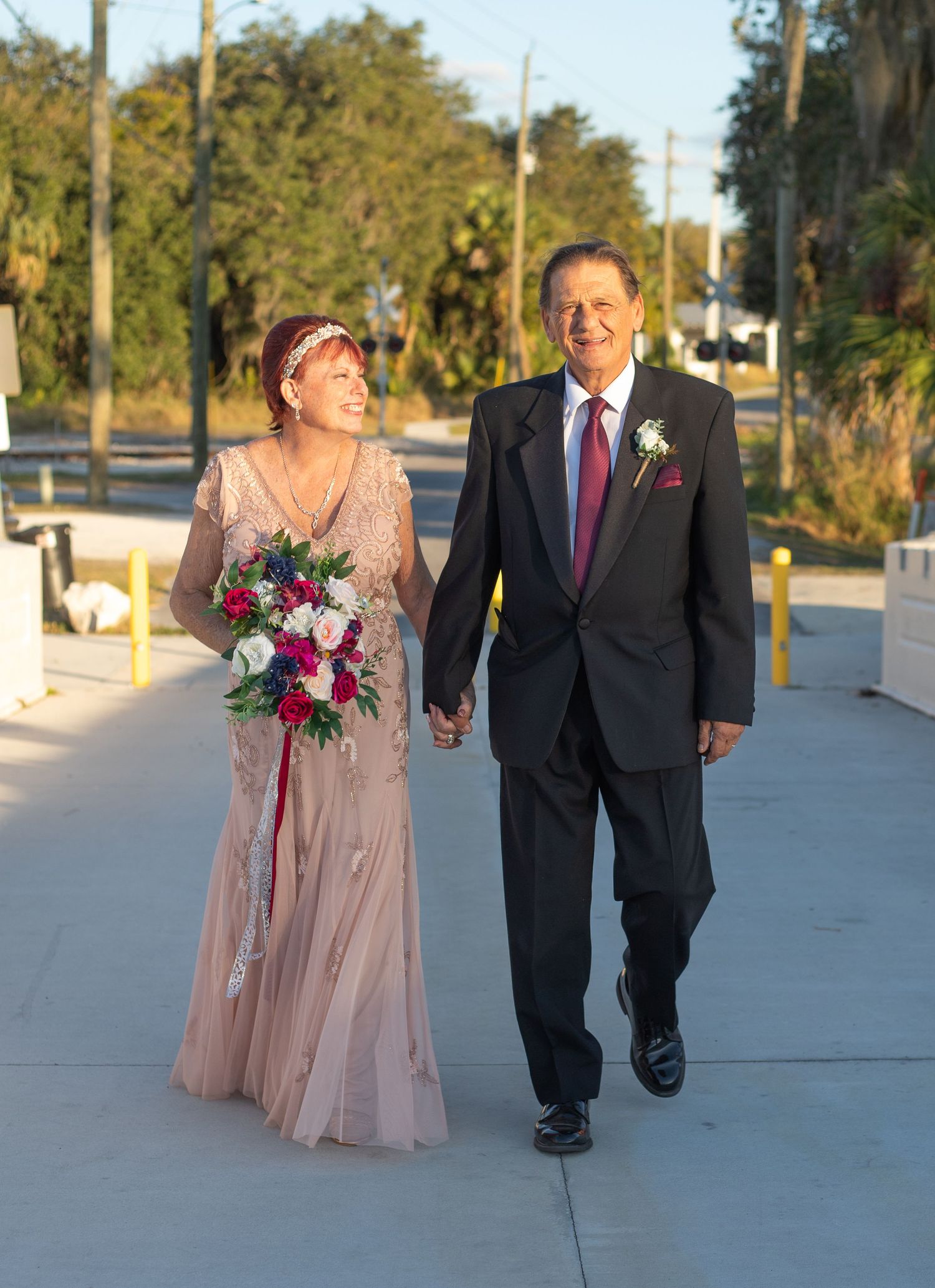 Couple walking together on concrete path during sunset wedding photoshoot.