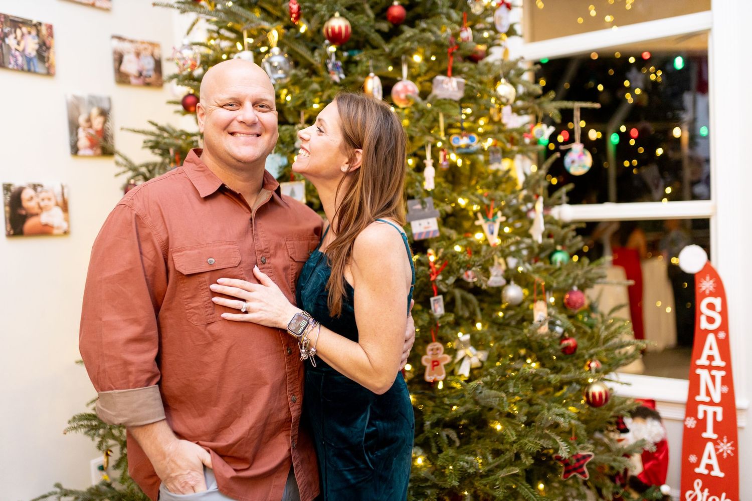 Candid holiday portrait session with decorated Christmas tree and Santa decorations in background.