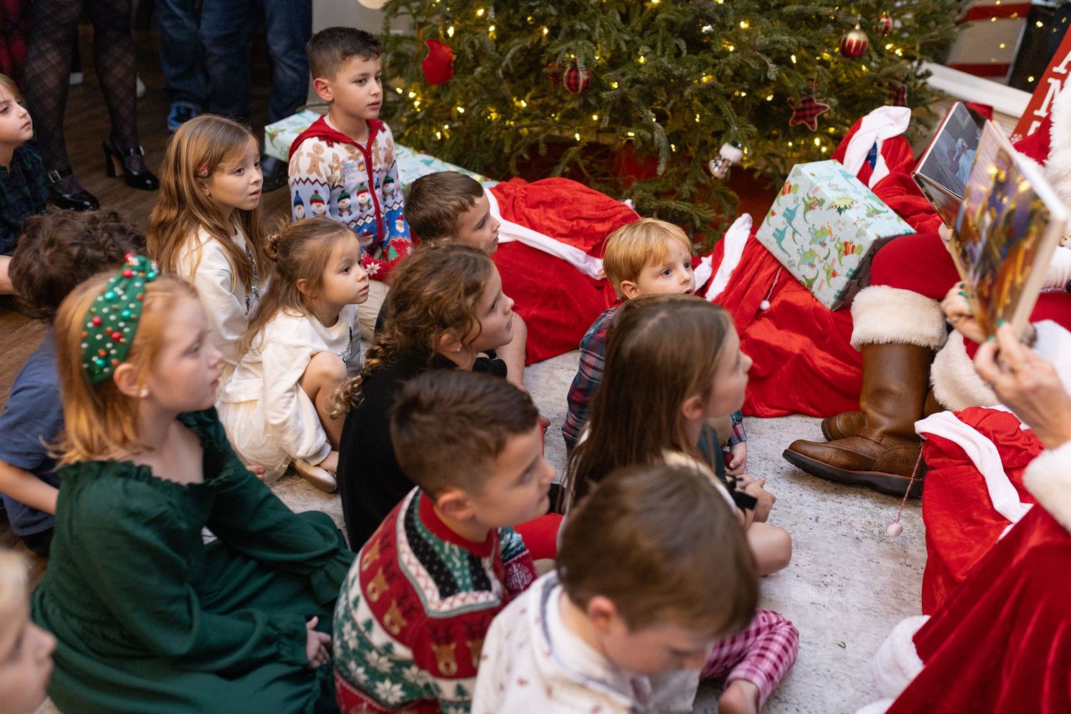 Children gather around a Christmas tree during a holiday celebration.