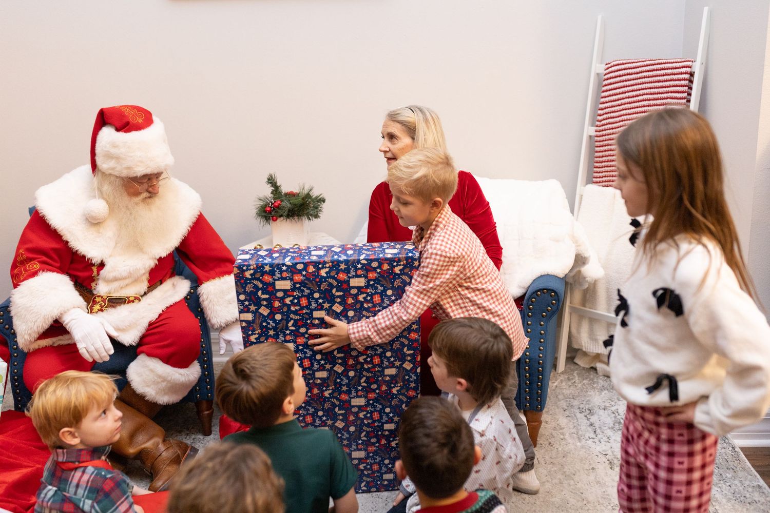 Children and adults gather around Santa Claus during a holiday celebration indoors.