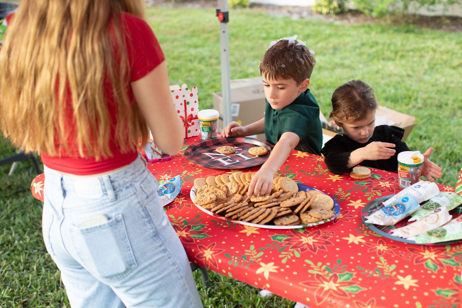 Group enjoying an outdoor holiday party with festive red tablecloth and food spread.