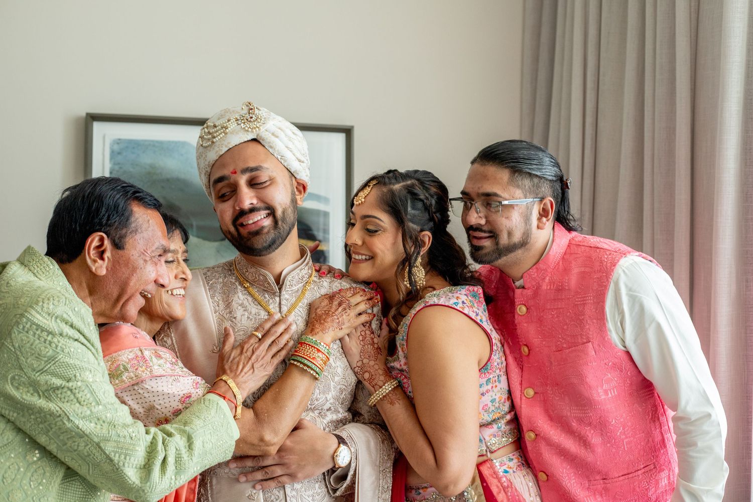 Indian groom in white sherwani and turban shares joyful moment with family during traditional wedding celebration.