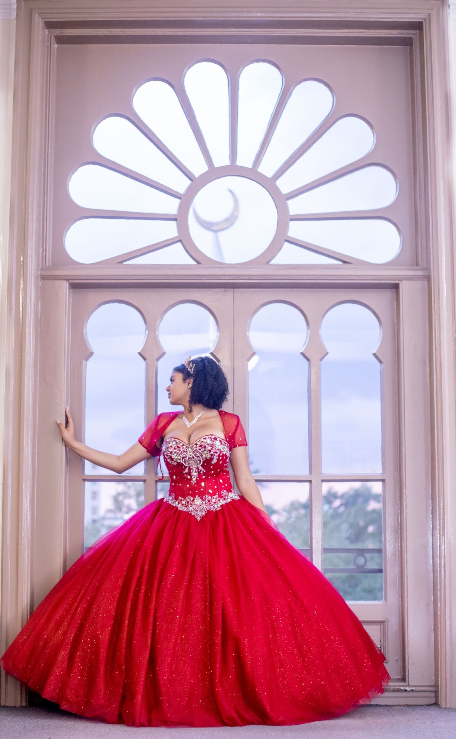 Flowing red ballgown photographed against ornate white fan windows.