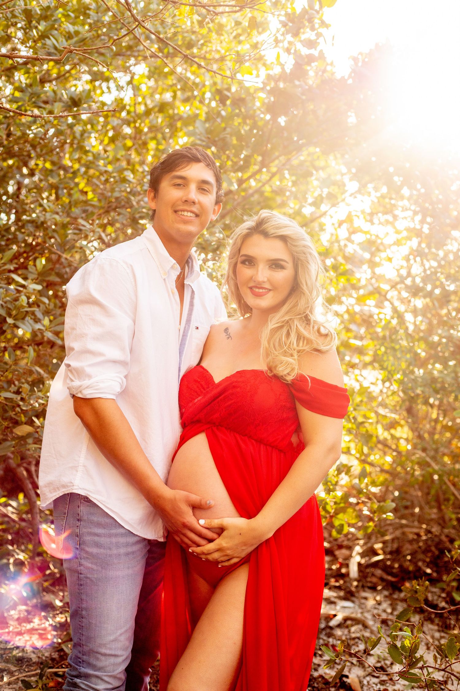 Romantic maternity photoshoot at sunset with couple embracing near water.