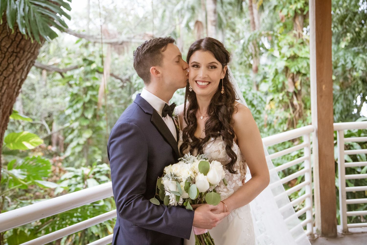 Joyful wedding couple portraits under a wooden pergola surrounded by lush greenery.