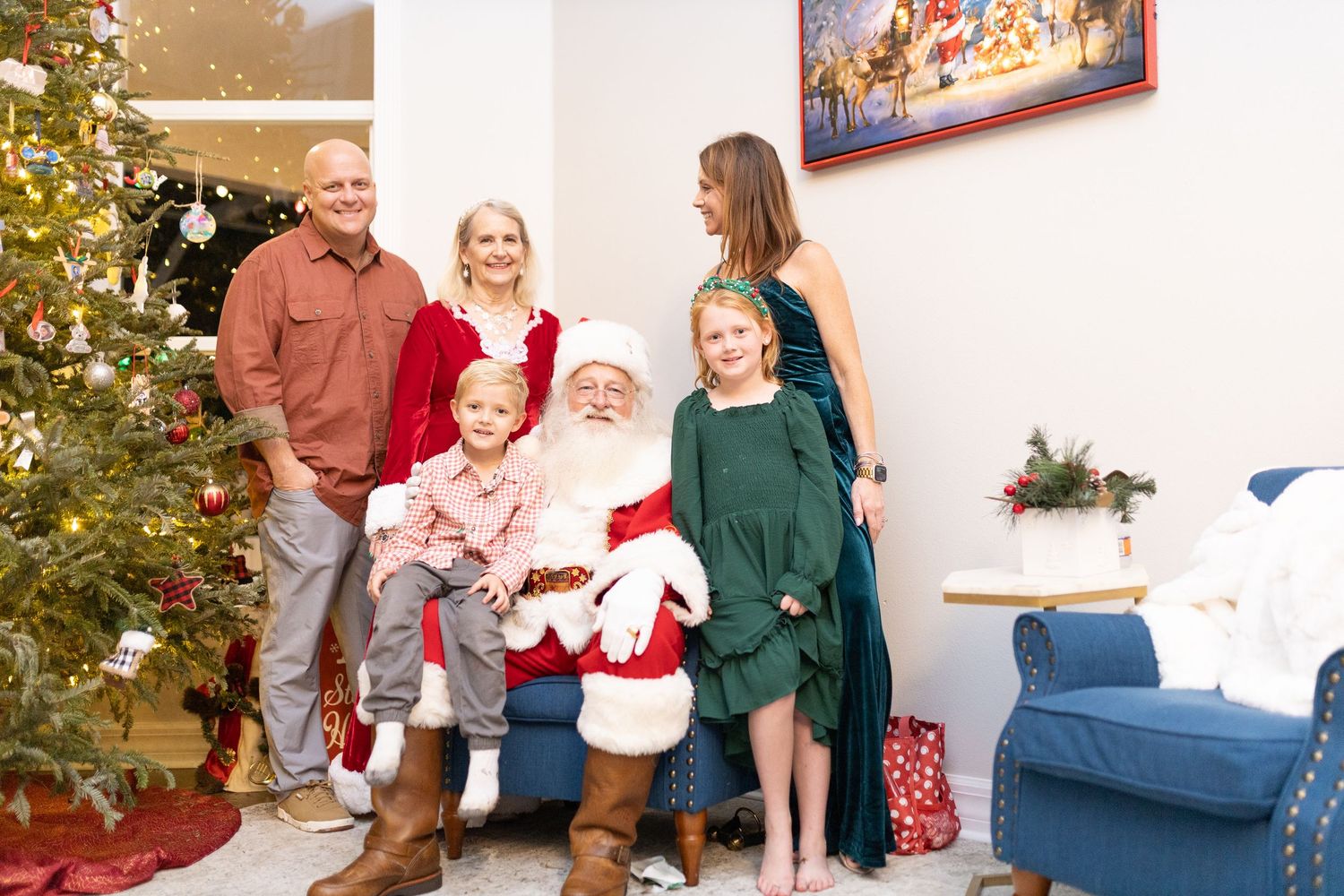 Family poses in coordinated outfits by decorated Christmas tree in living room with festive decor.