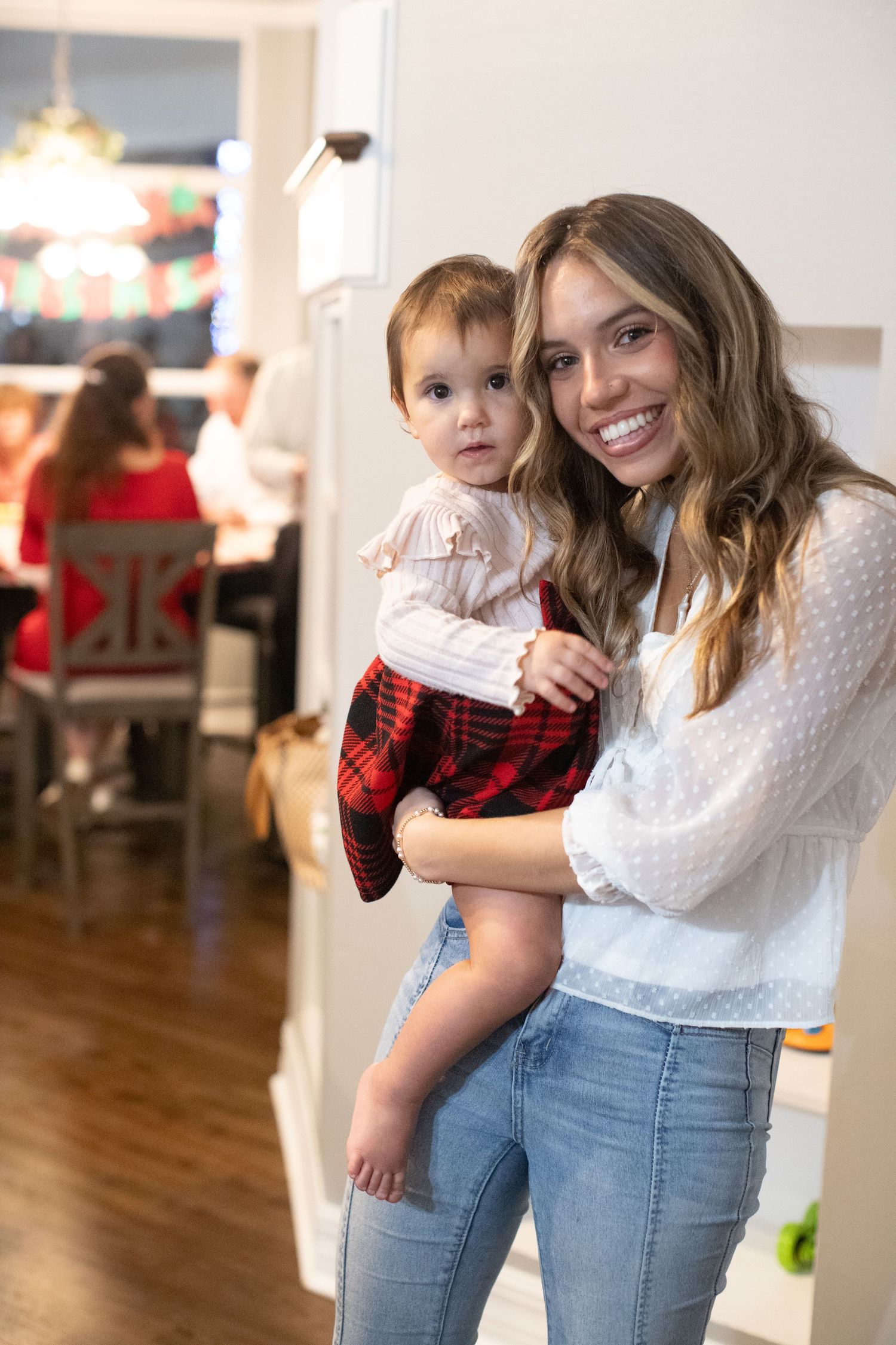 Indoor portrait showing a warm embrace between two people wearing casual clothing against a white wall.