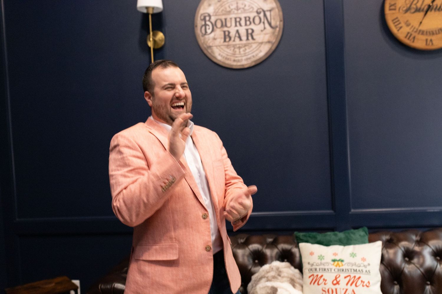 Person in a peach-colored suit jacket speaking animatedly in front of a bourbon bar sign.