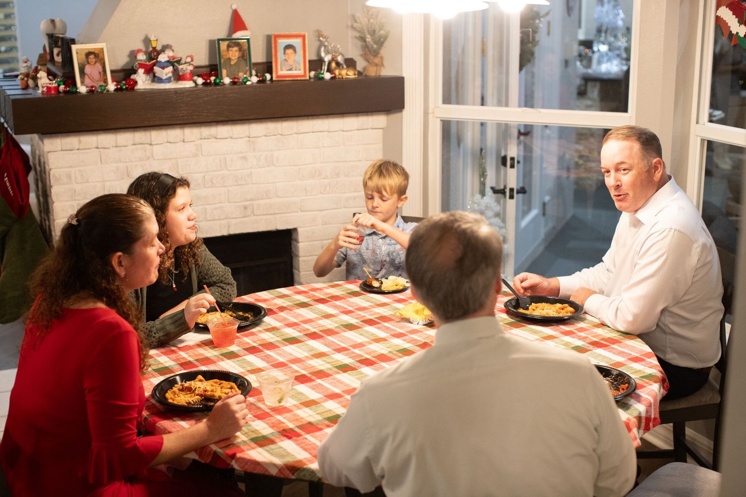 Indoor dining scene with red checkered tablecloth and people gathered around for a meal.
