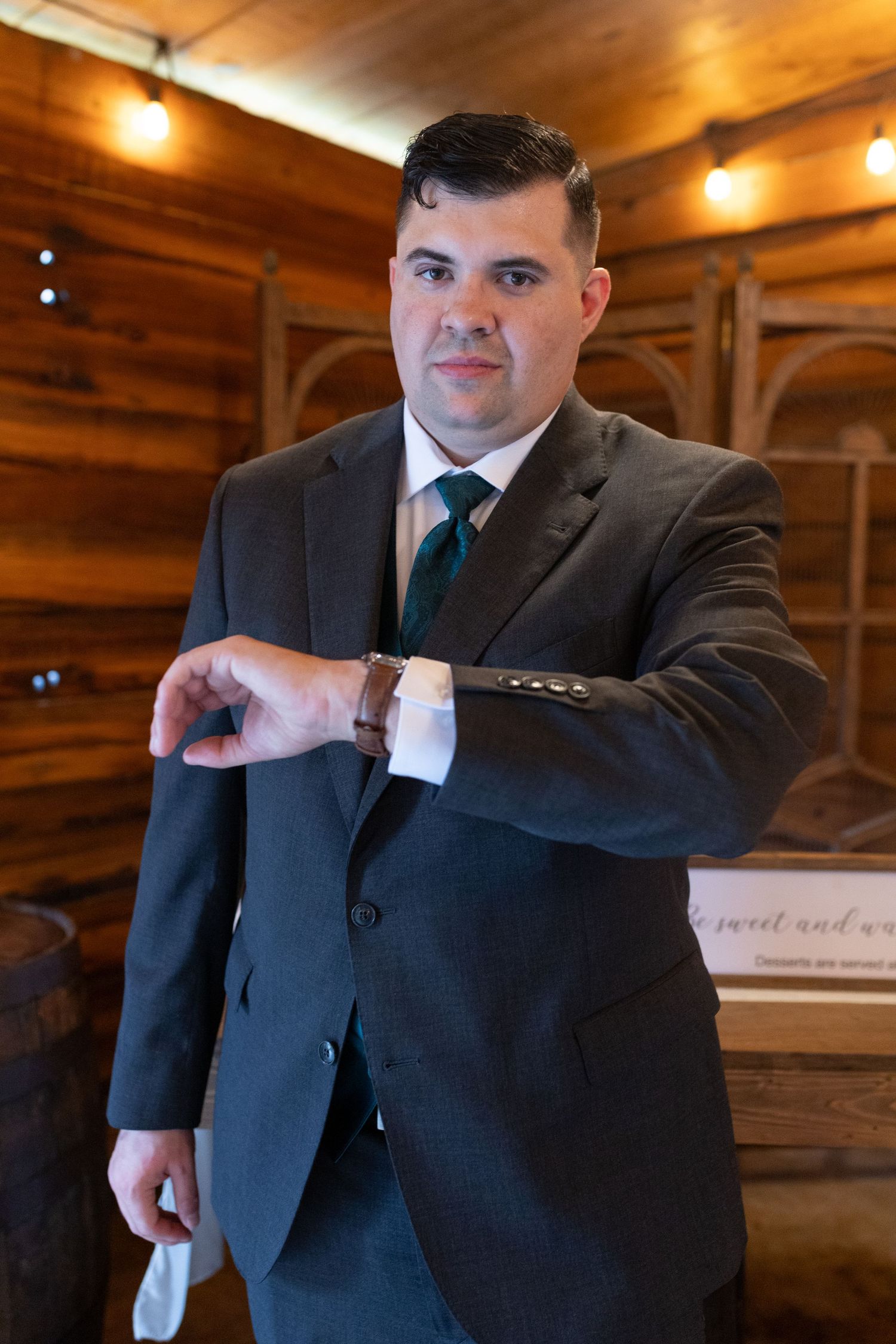 Groom in a dark suit makes playful gestures in a rustic wooden venue.