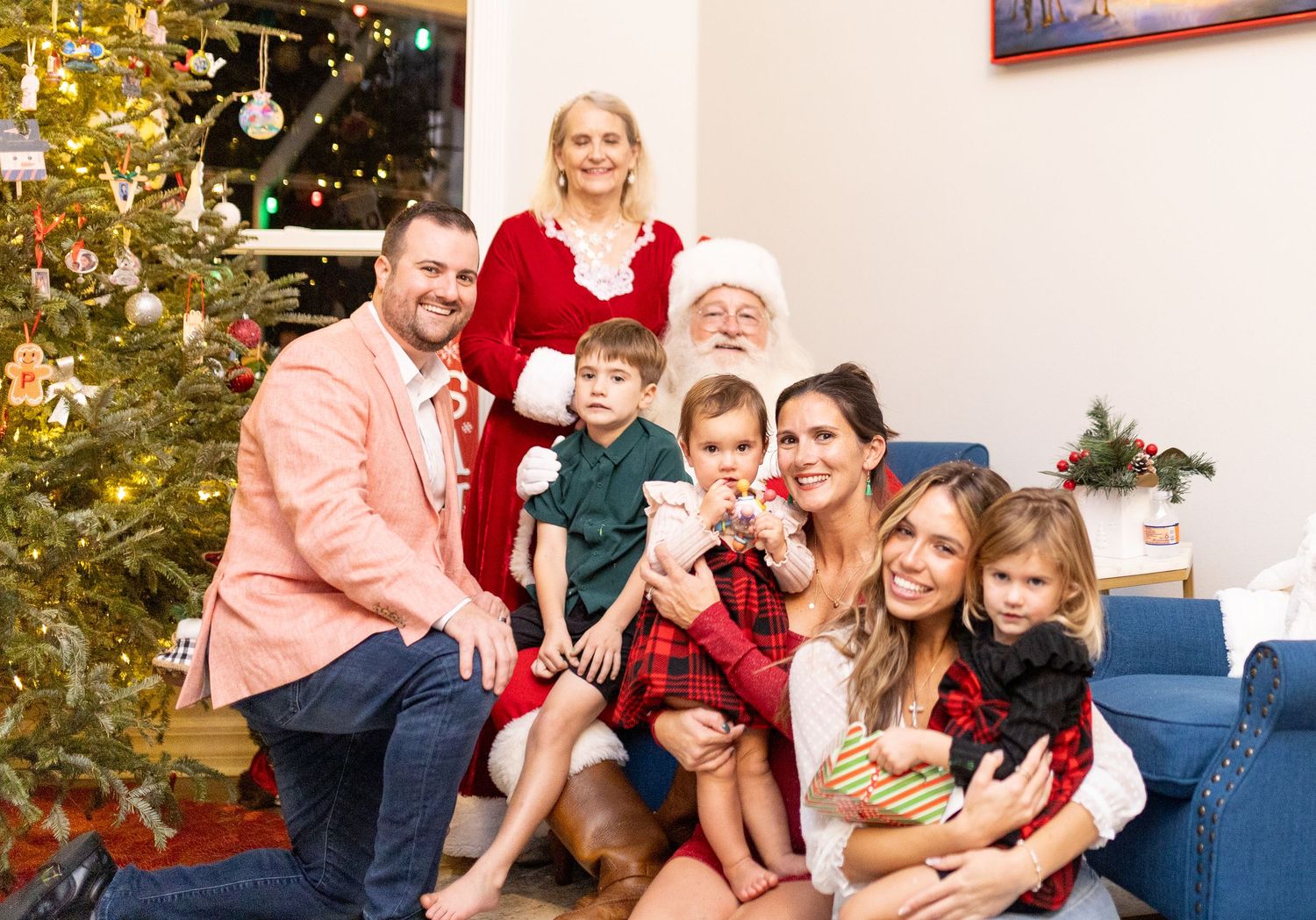Holiday photo session with family and Santa Claus by decorated Christmas tree and blue couch.