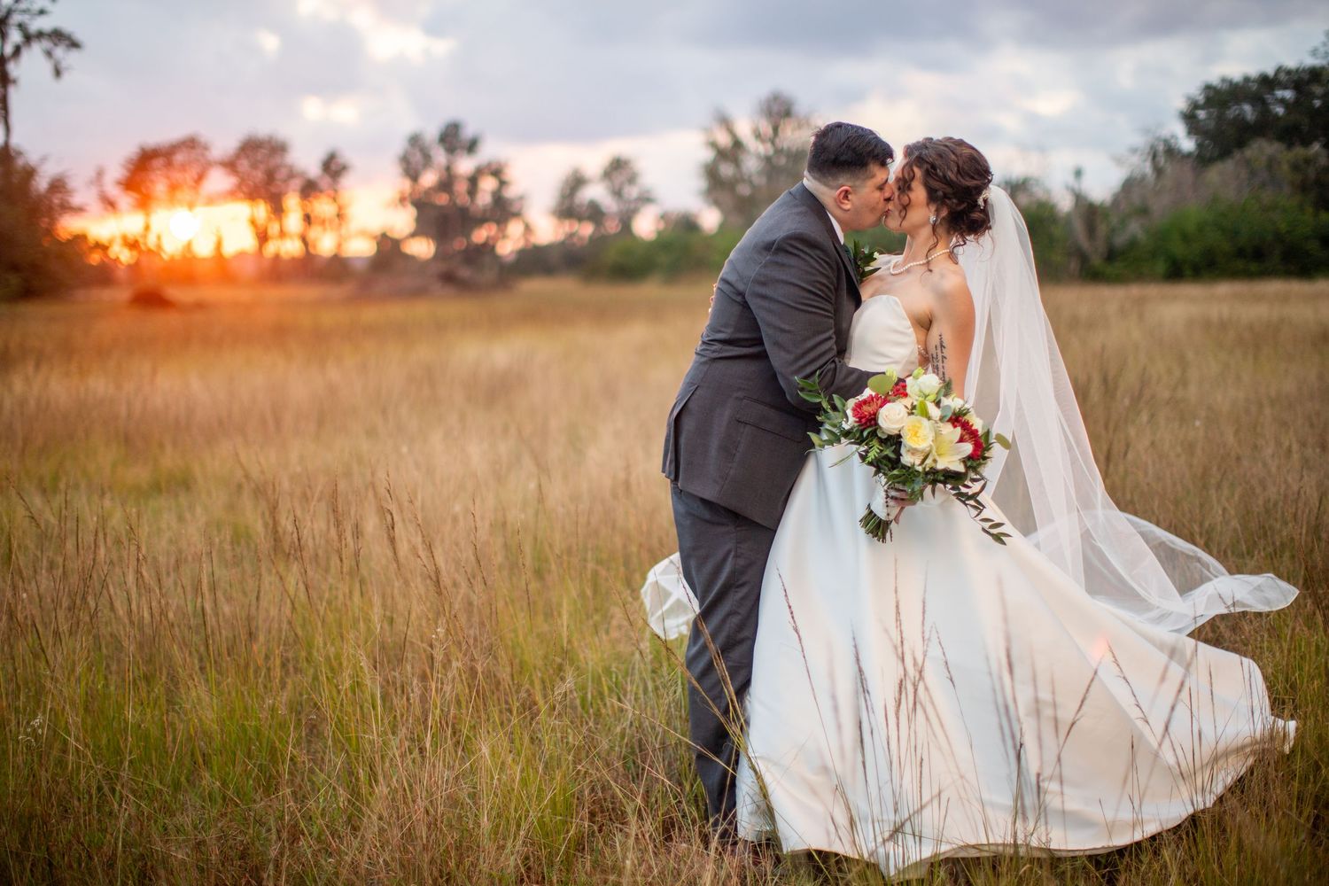 Romantic sunset wedding photography session in a golden field with flowing white dress and floral bouquet.