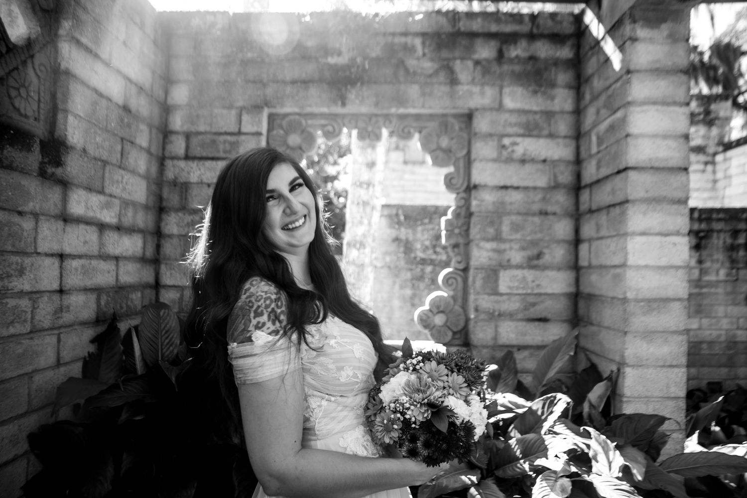 Black and white photo of a smiling bride holding a bouquet in a rustic stone setting.