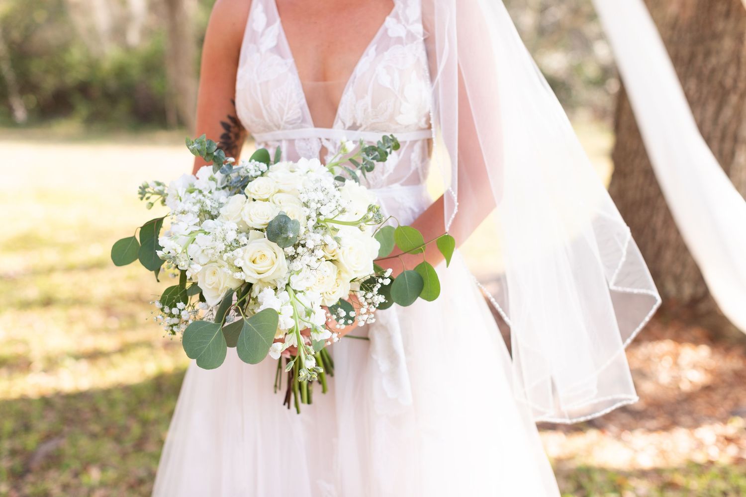 Close-up of bridal bouquet featuring white flowers and eucalyptus leaves against white wedding dress.