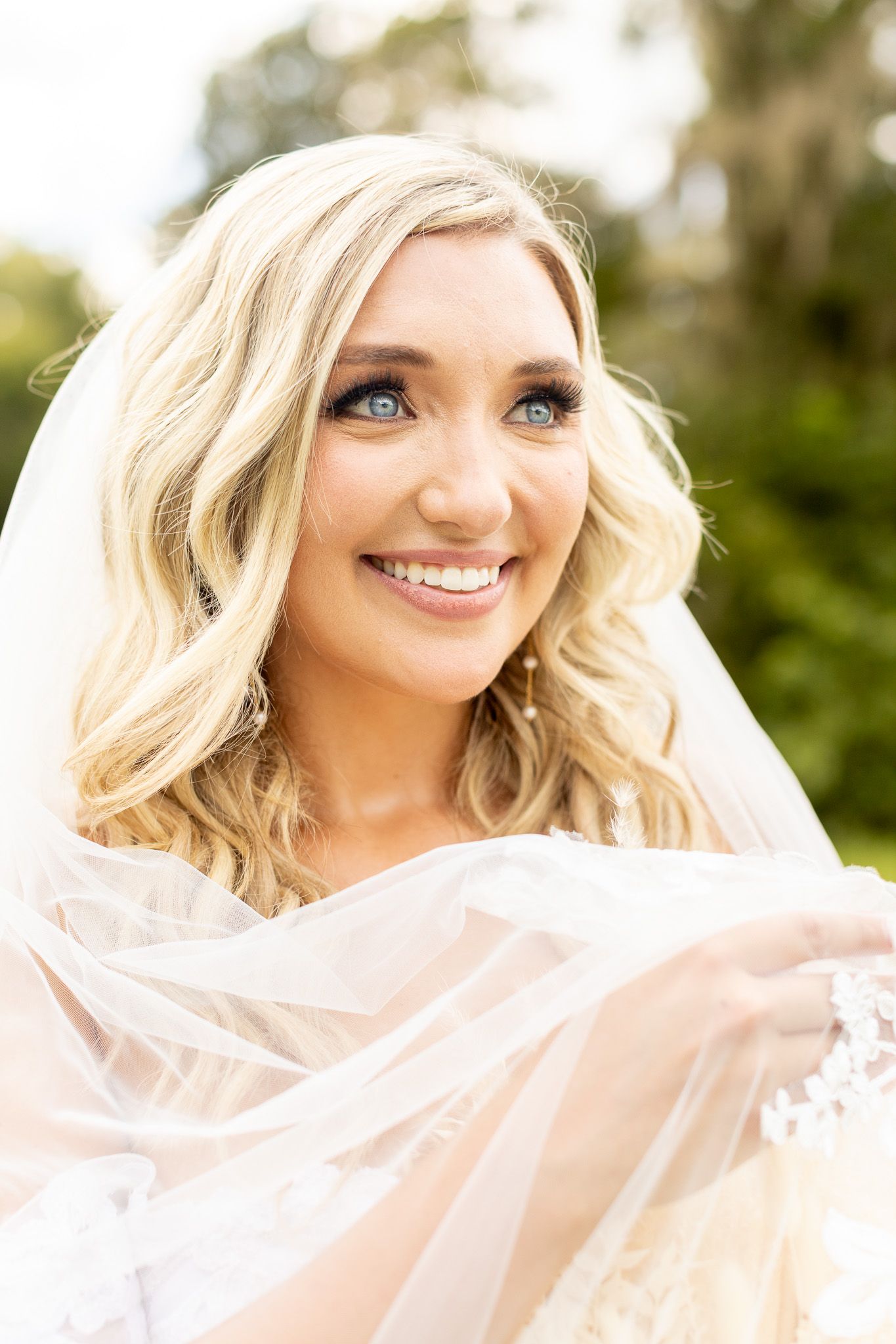 Joyful bridal portraits with flowing veil and natural lighting in outdoor setting.